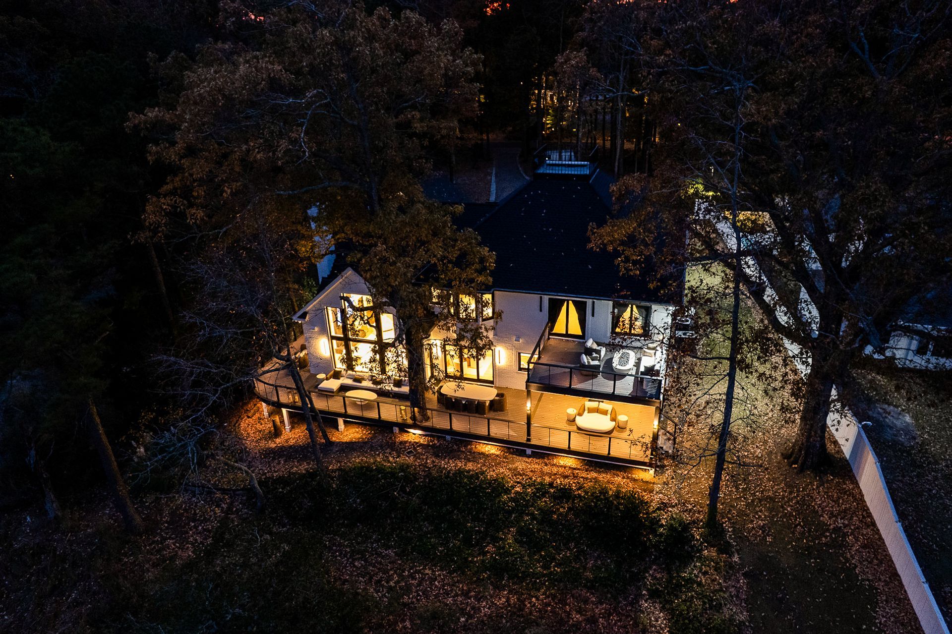 A two-story house at night, lit from within, surrounded by dark trees.