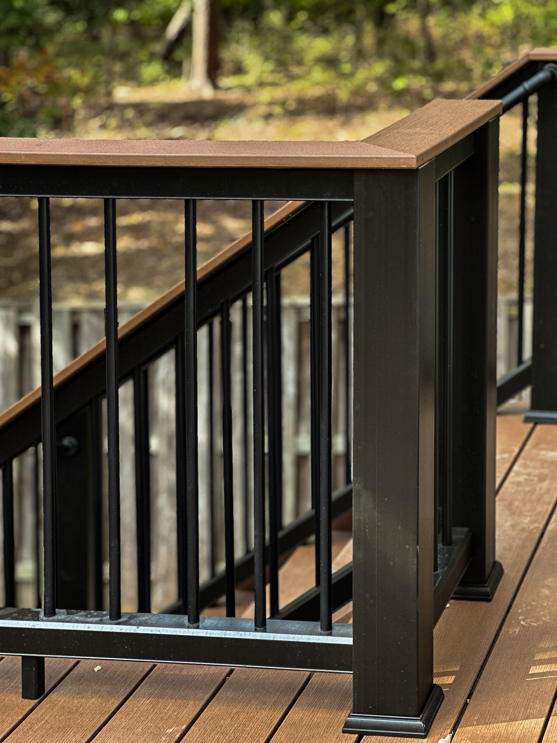 Black deck railing with brown top rail and vertical black bars, on a brown deck.