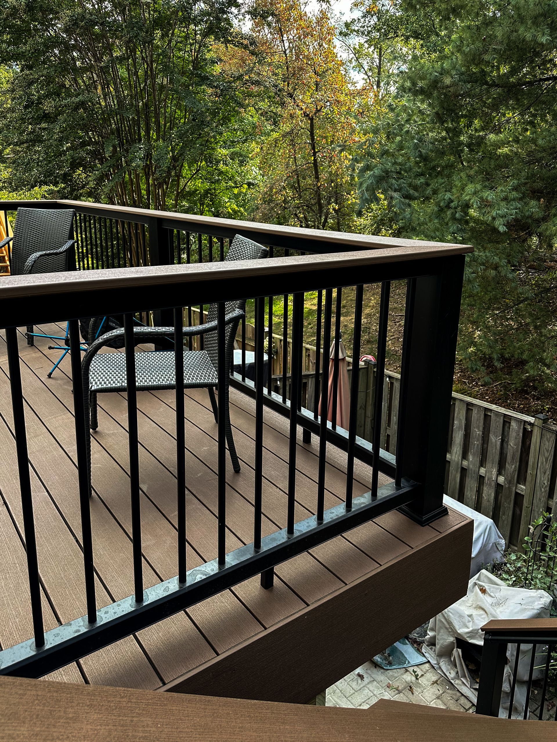 Deck with black railing, brown composite decking, outdoor seating. Trees in background.