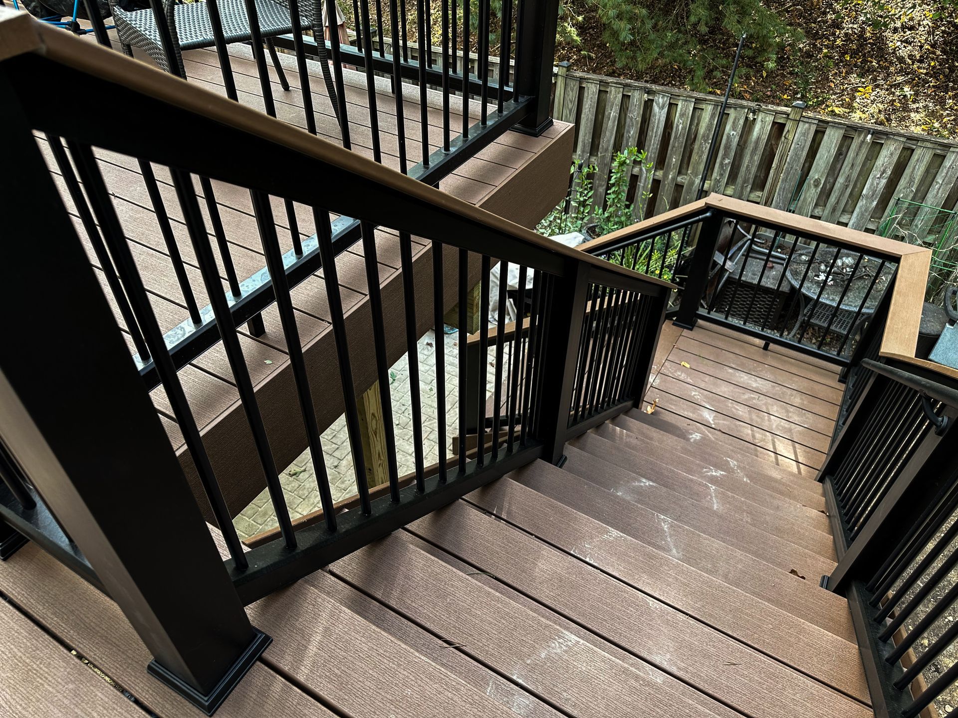 Stairs with brown composite decking and black metal railings leading down to a deck with outdoor furniture.
