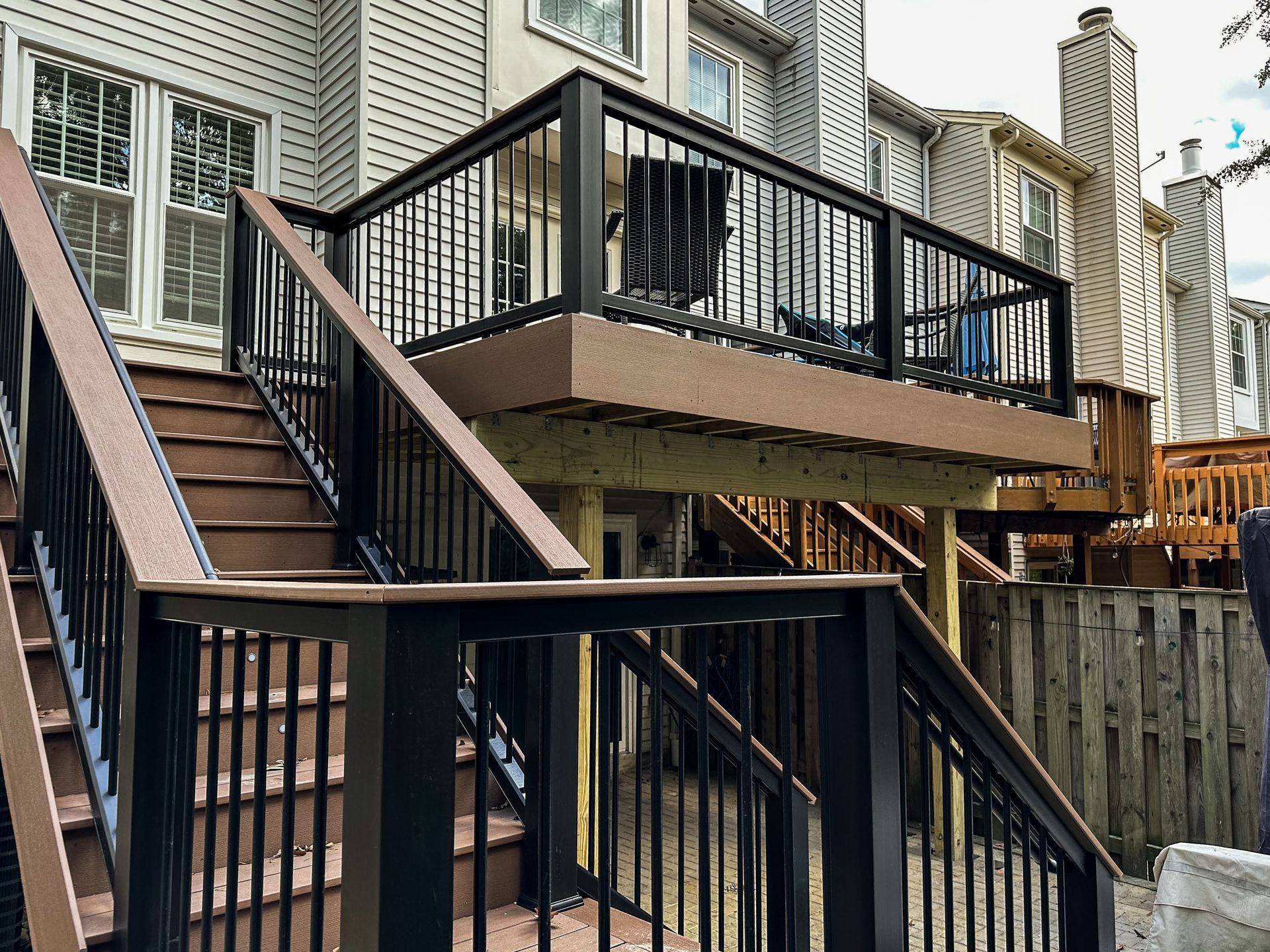 Multi-level deck with black railing and brown stairs attached to a house with beige siding.