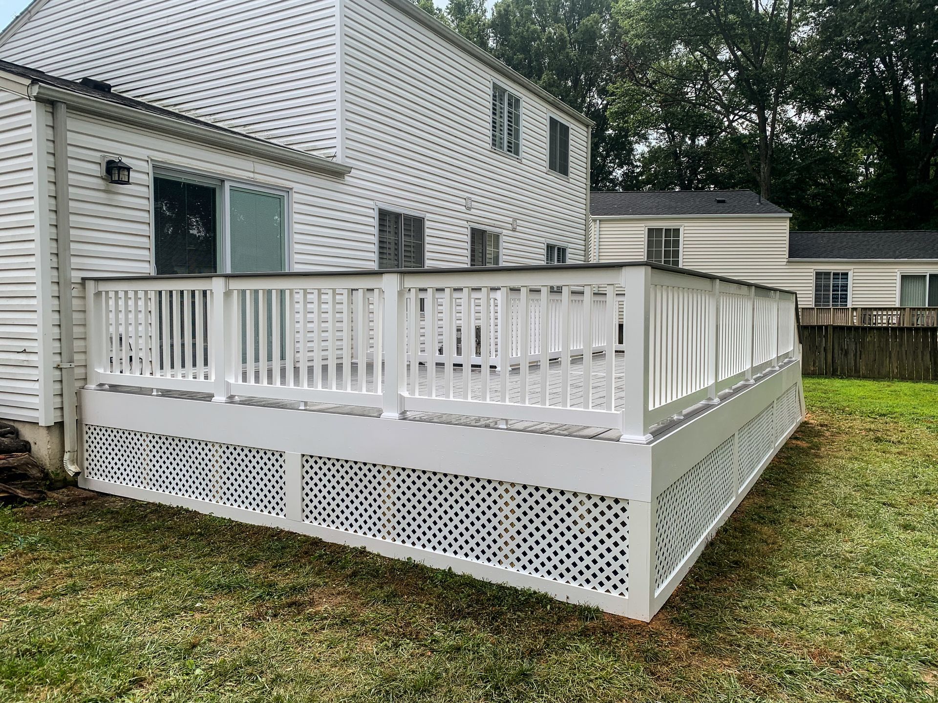 White deck attached to a two-story house with lattice skirting and a grassy yard.
