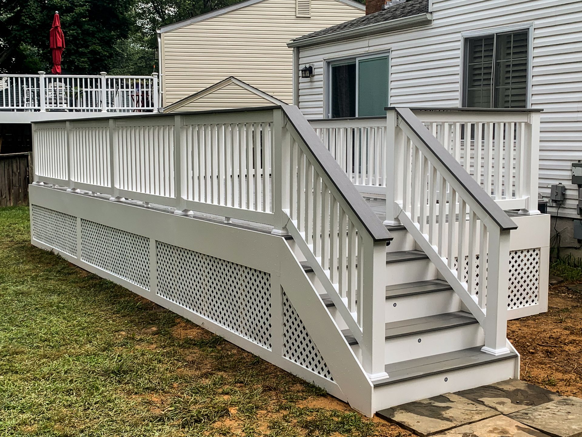 White deck with stairs, lattice detail, and white railing, in a backyard setting.