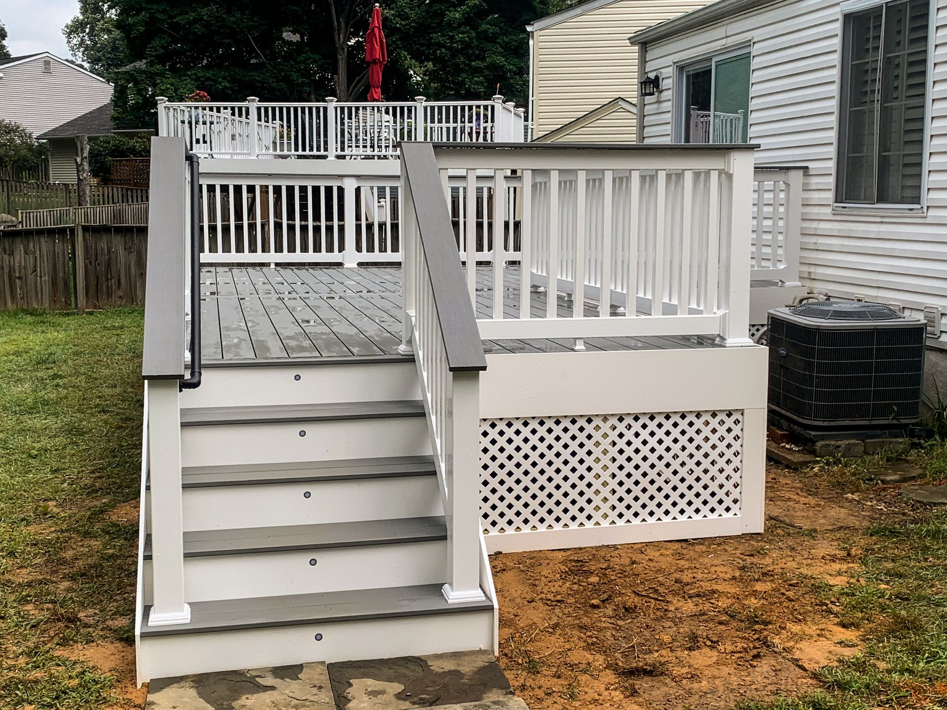 Gray and white deck with steps, railing, and lattice, adjacent to a house.