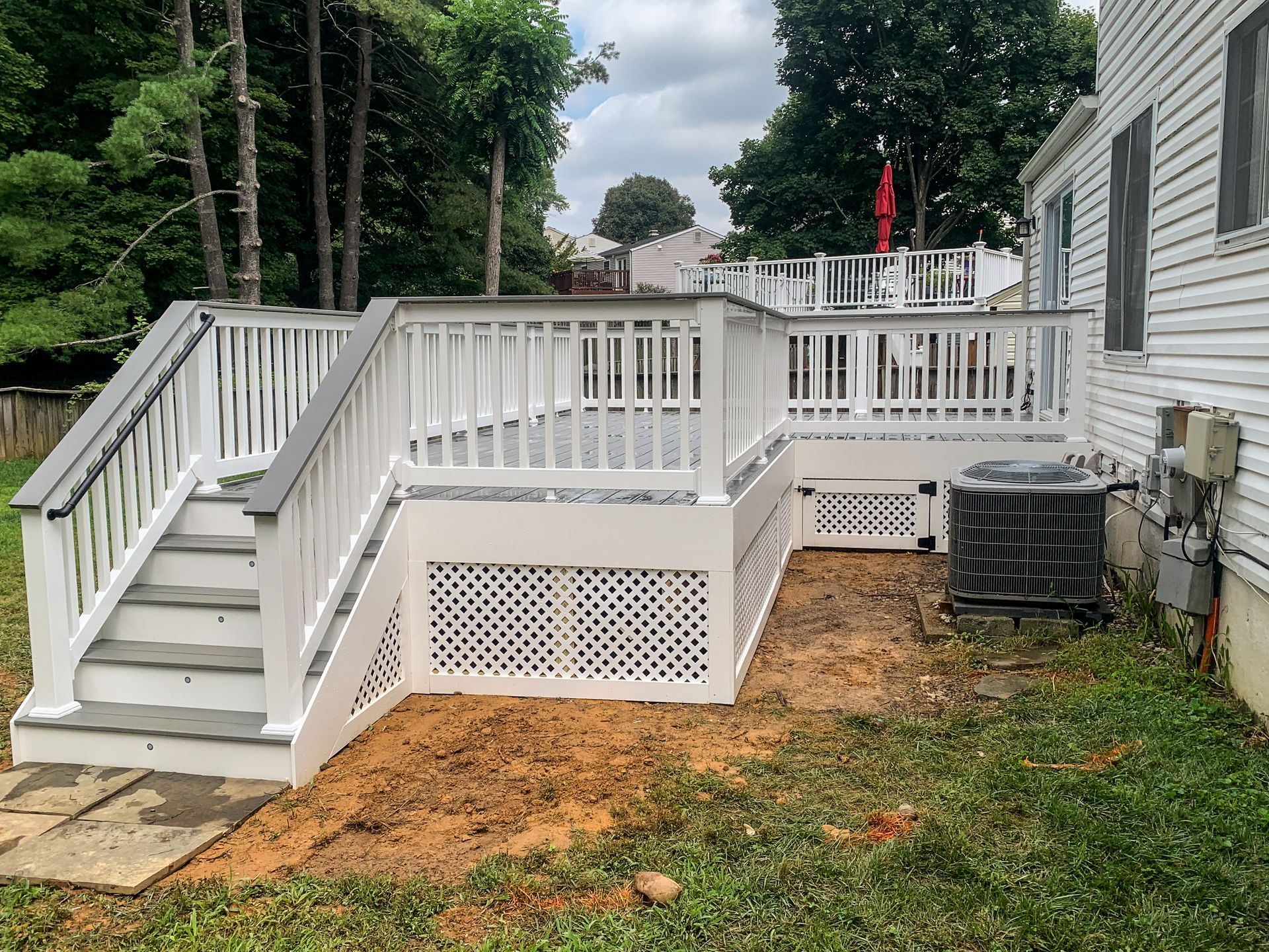 White deck with stairs, lattice skirting, next to a house with an air conditioner unit on the side.