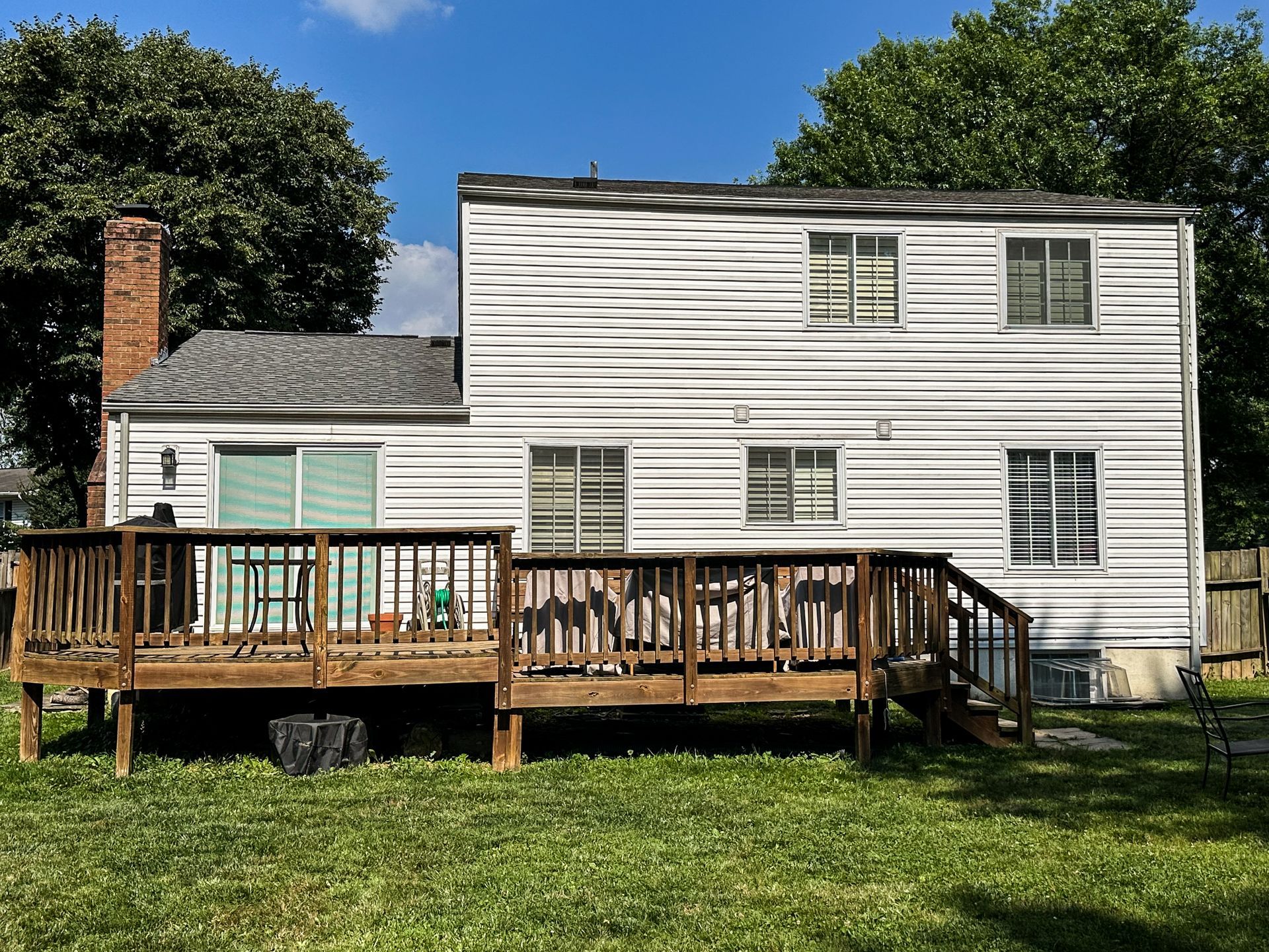 Back of a two-story white house with a brown wooden deck and green lawn. A brick chimney is visible.