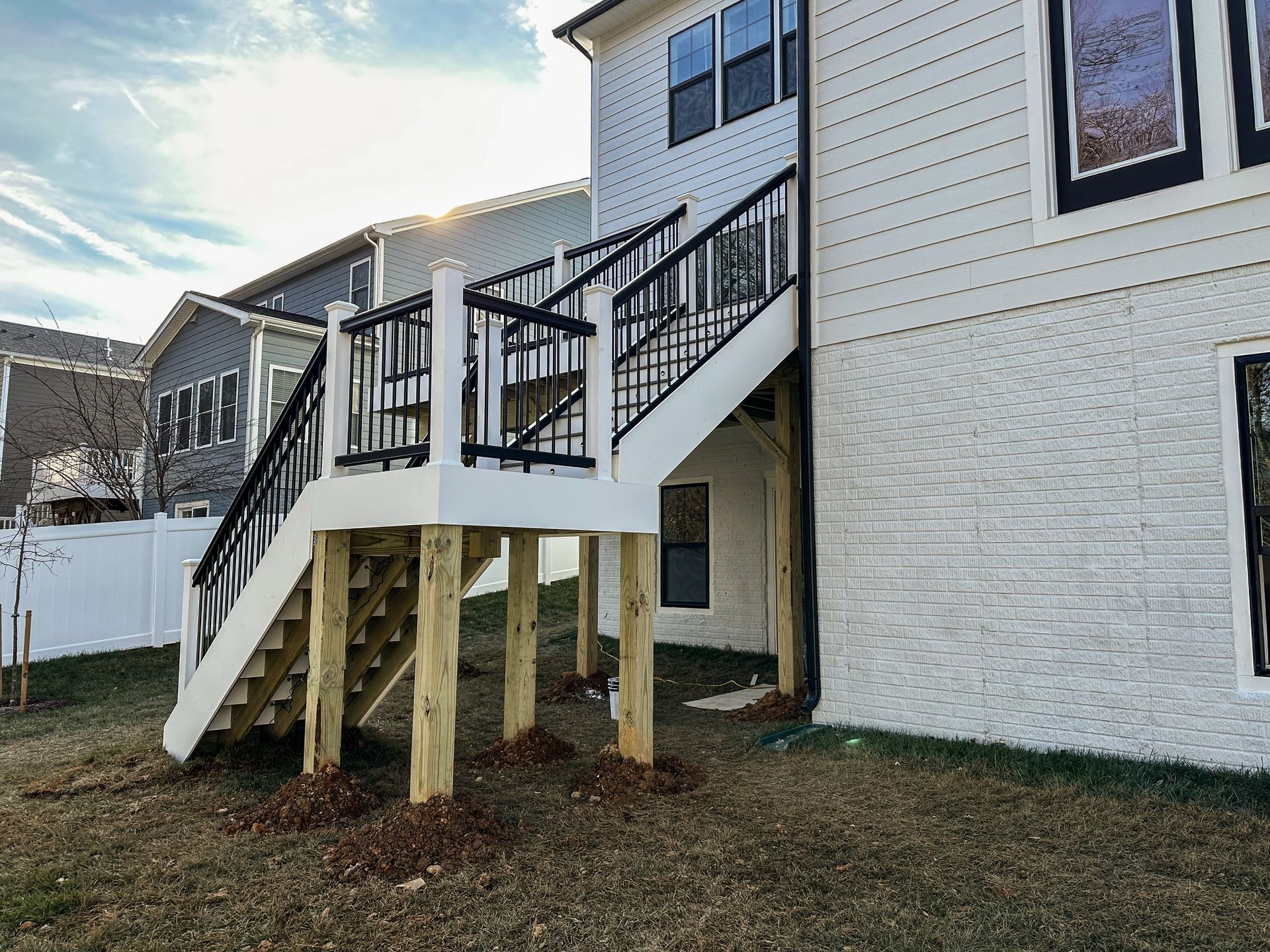 White deck with black railings and stairs attached to a two-story white brick house.