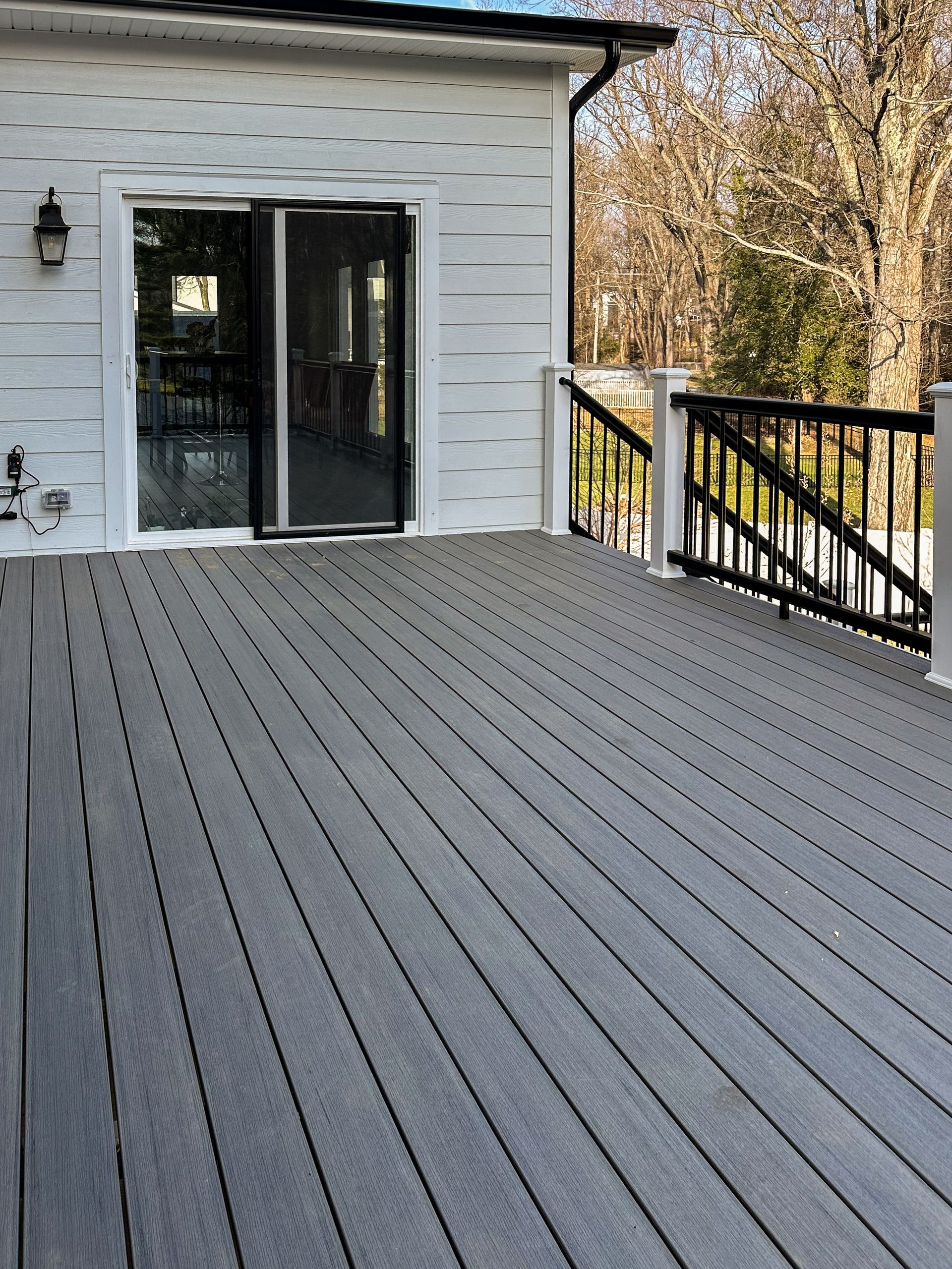 Gray composite deck with a sliding glass door and black railing. White house exterior.