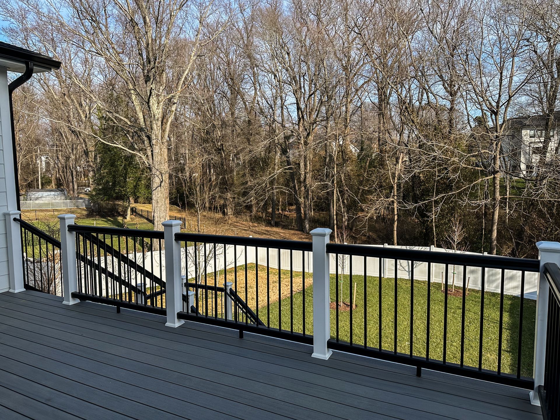 Deck with black railing, white posts, and gray decking, overlooking a backyard with trees.