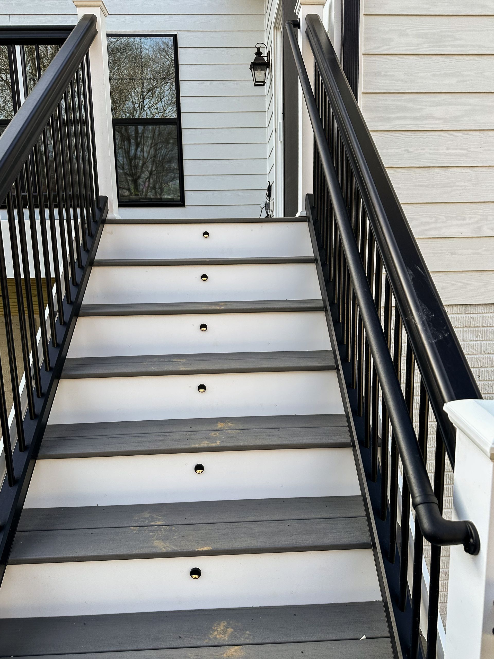 Outdoor stairway with black railings and recessed lights on the steps, leading up to a house with a window.
