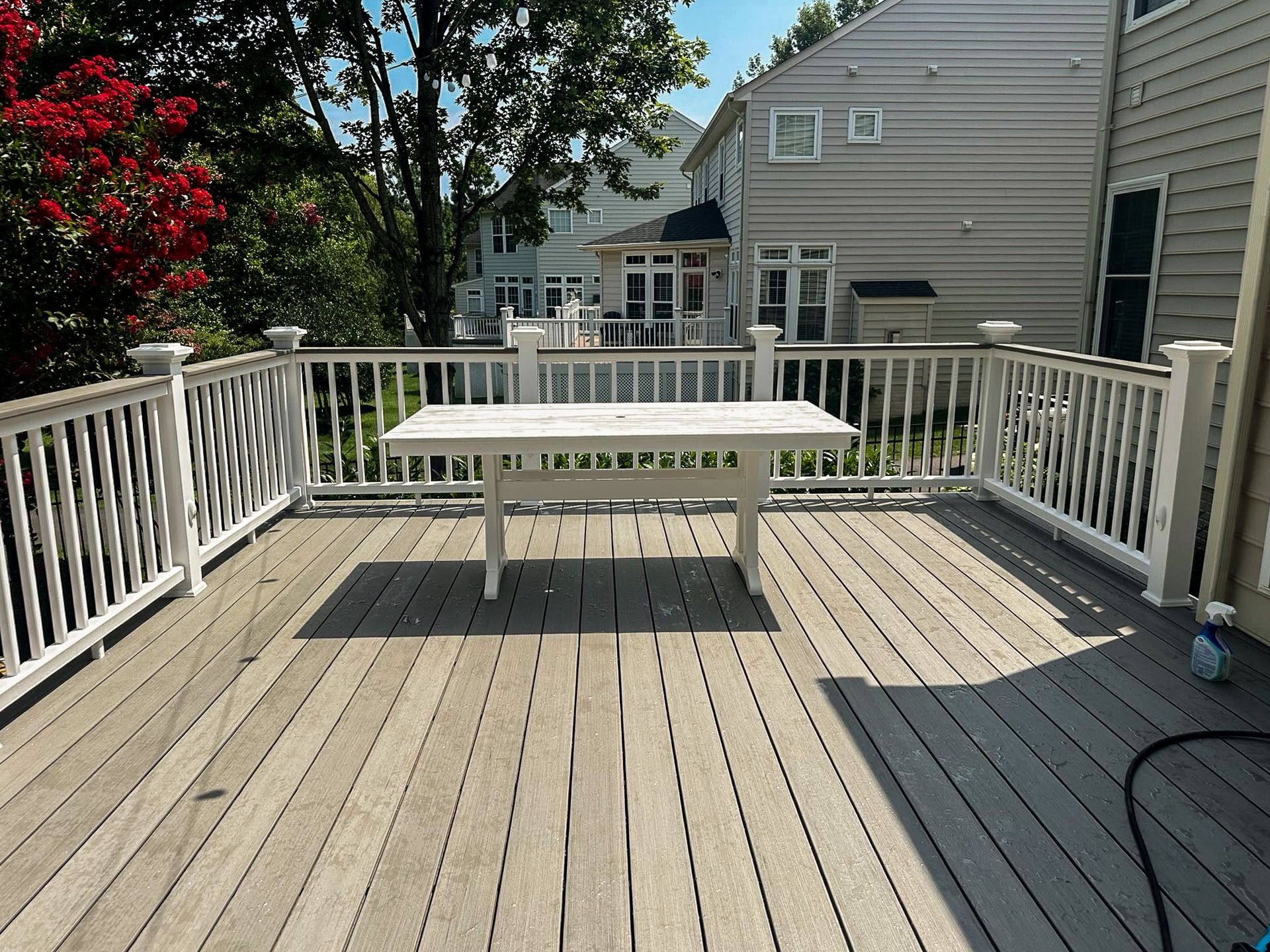Wooden deck with a white table; houses visible in the background on a sunny day.