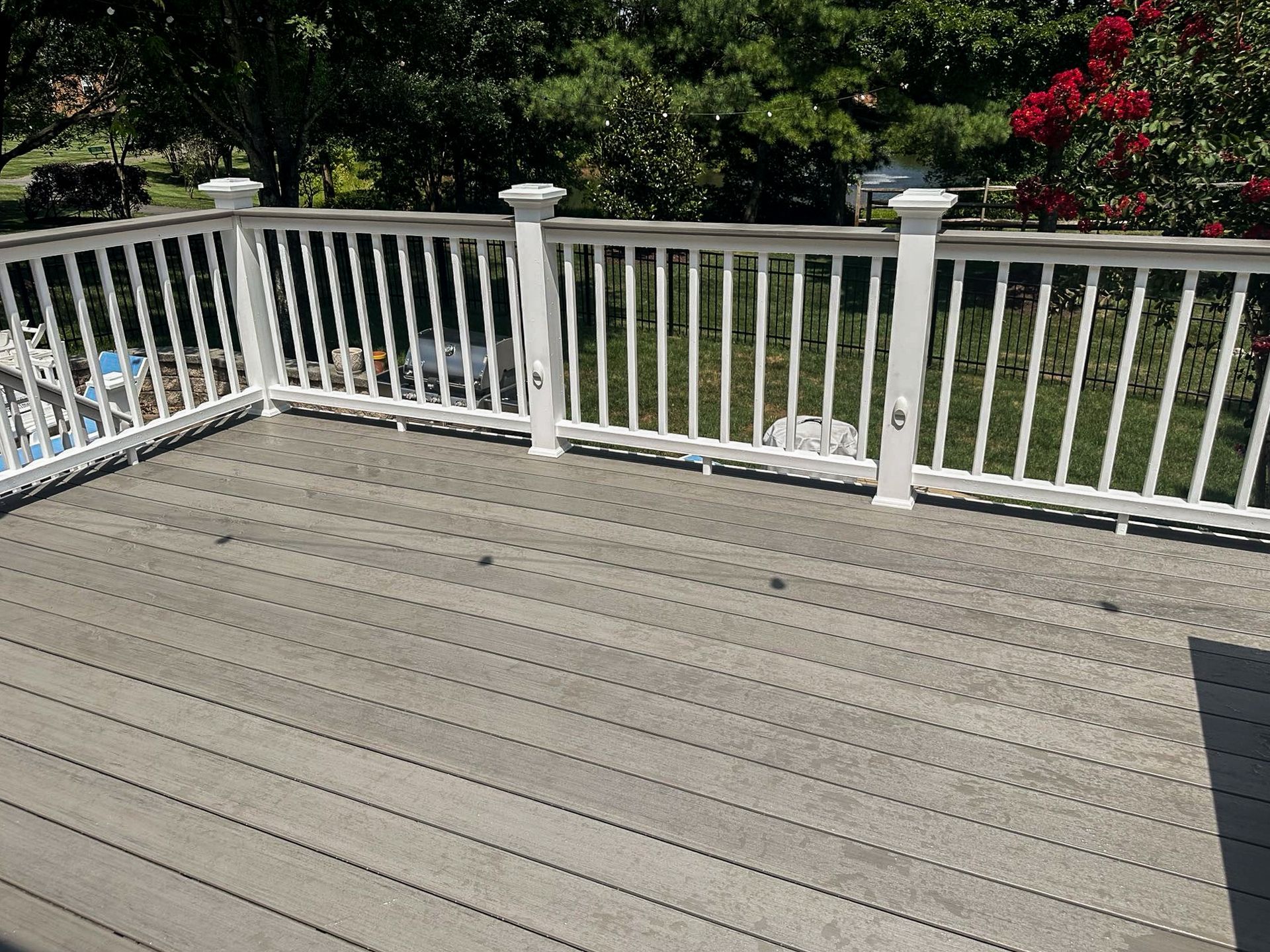 Gray composite deck with white railing, overlooking a green yard with trees and flowers.