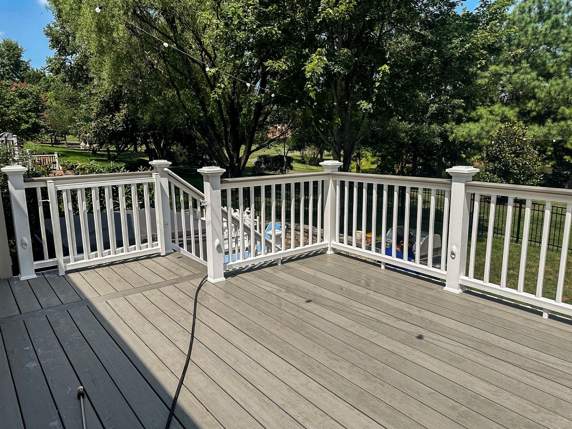 Wooden deck with white railing, gray decking, and green trees in the background.