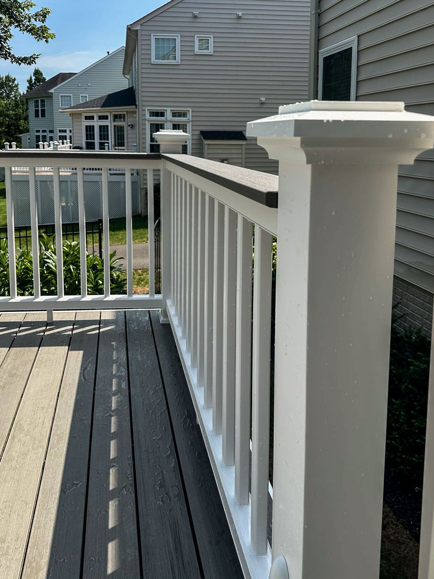 Composite deck railing with white posts, balusters, and gray decking, next to a house.