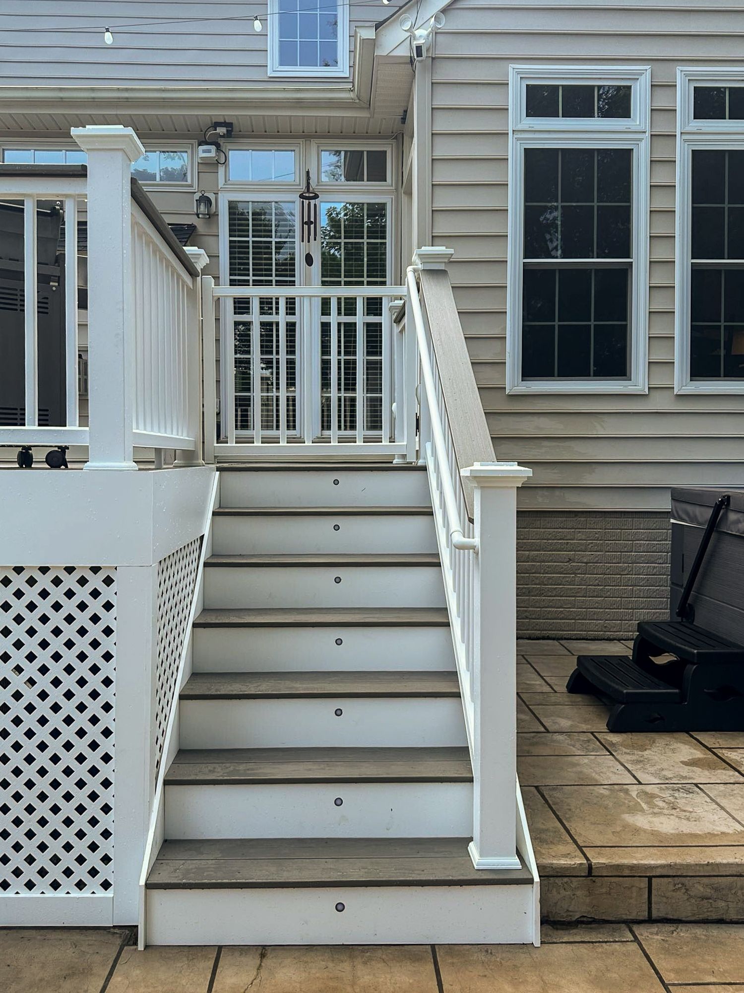 White stairs leading up to a door, on a deck with white railing. Cream-colored house in the background.