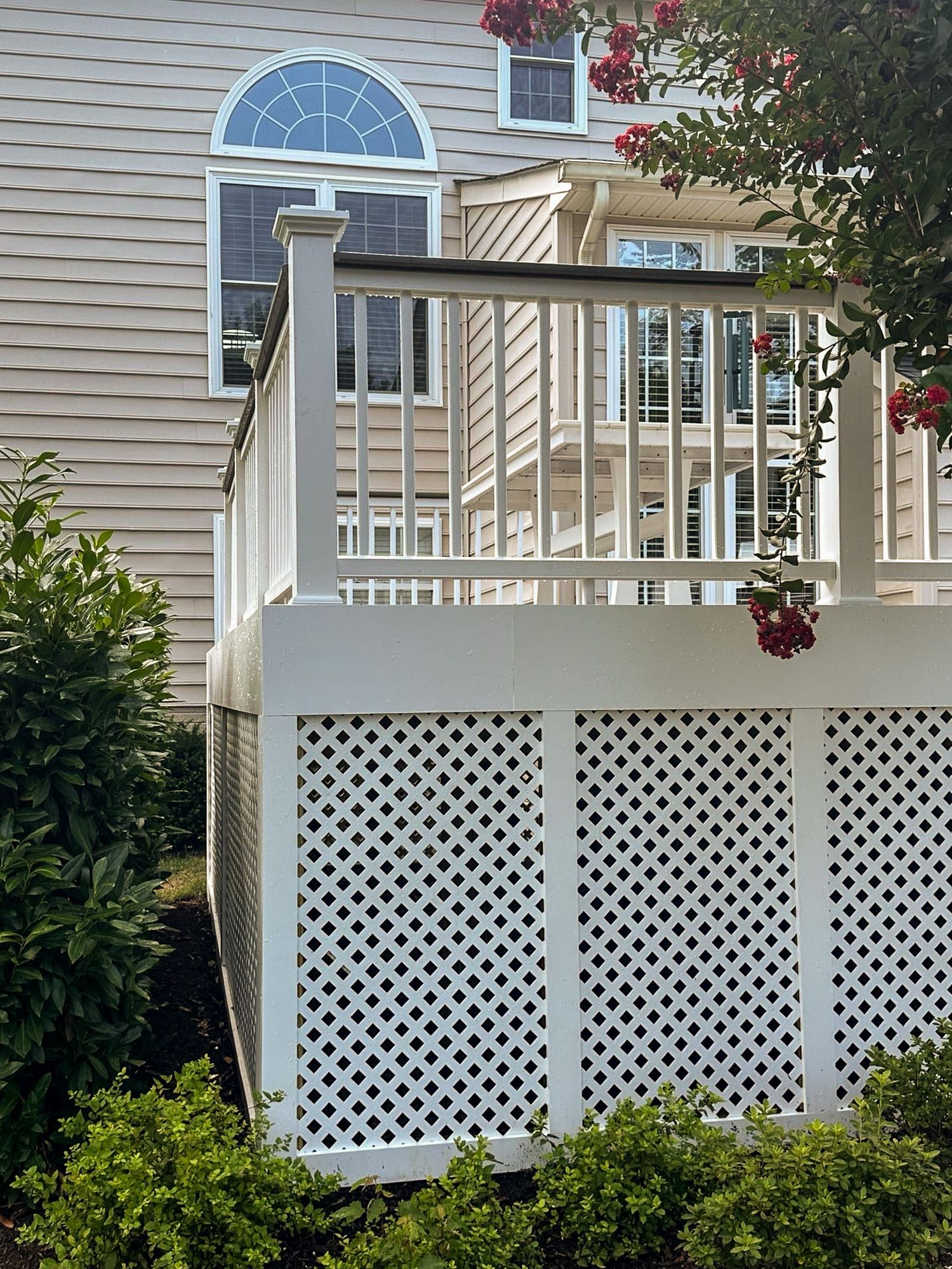 White deck with lattice skirting, topped with a railing. House with arched window visible behind.