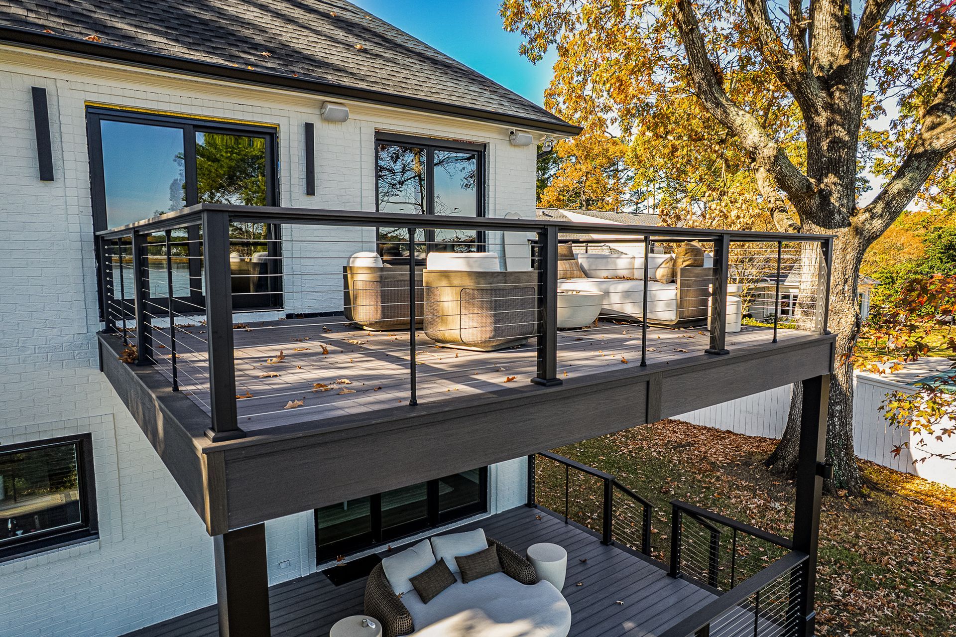 Elevated deck with hot tub, seating, and glass railings overlooking yard with fall foliage.