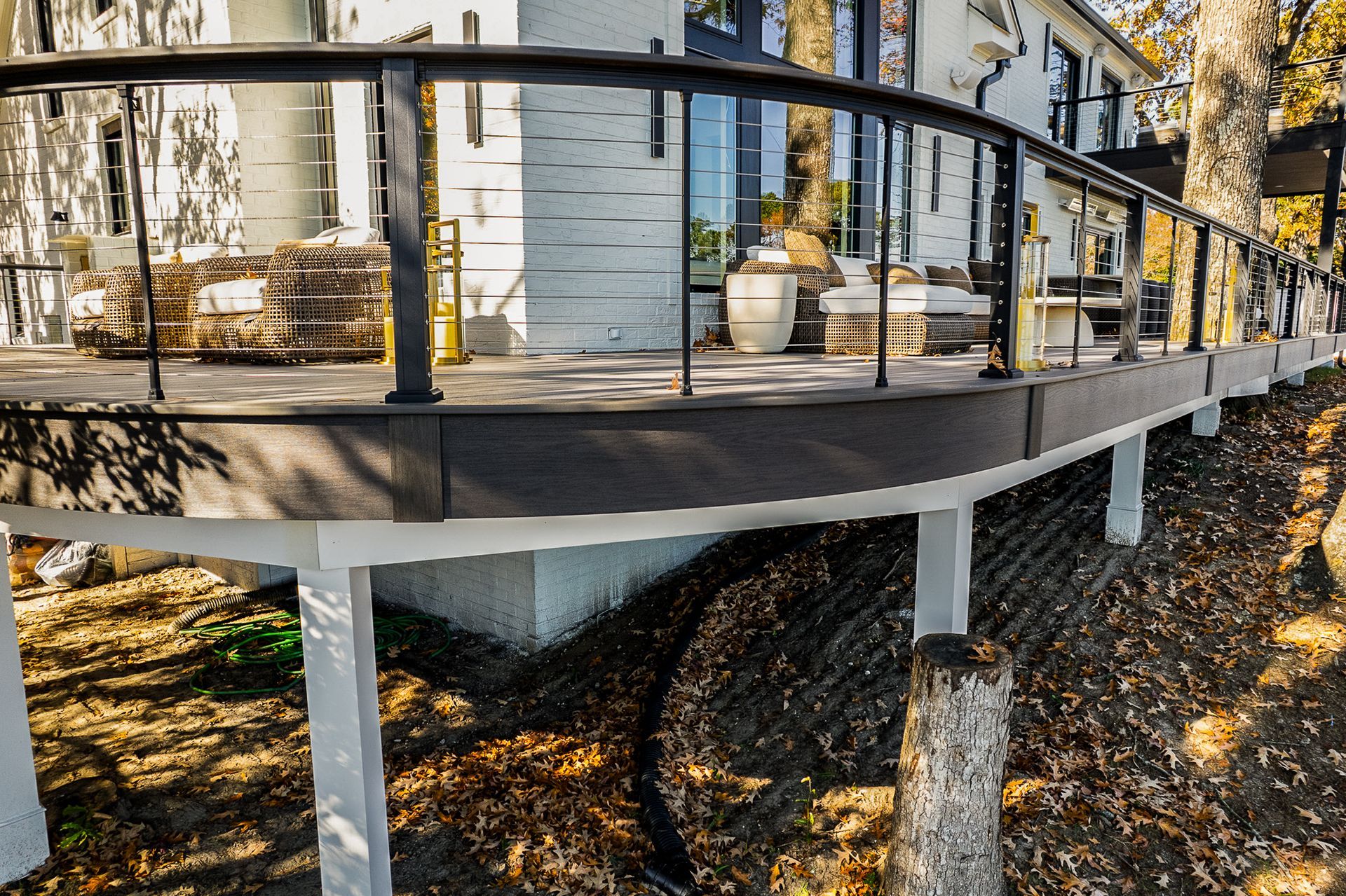 Curved black deck with glass railing, white support beams, and a house exterior.