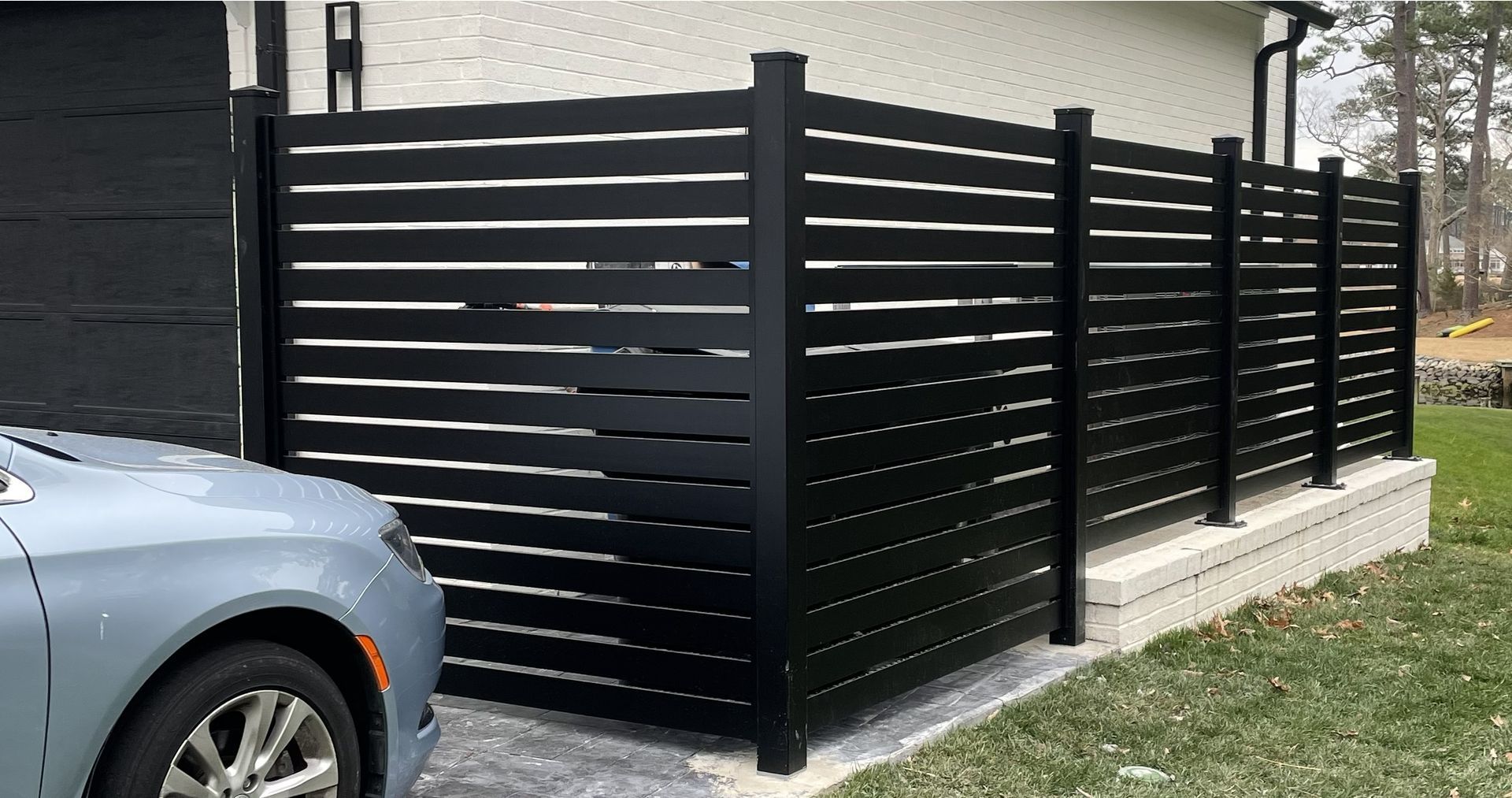 Black horizontal slat fence next to a building and car.