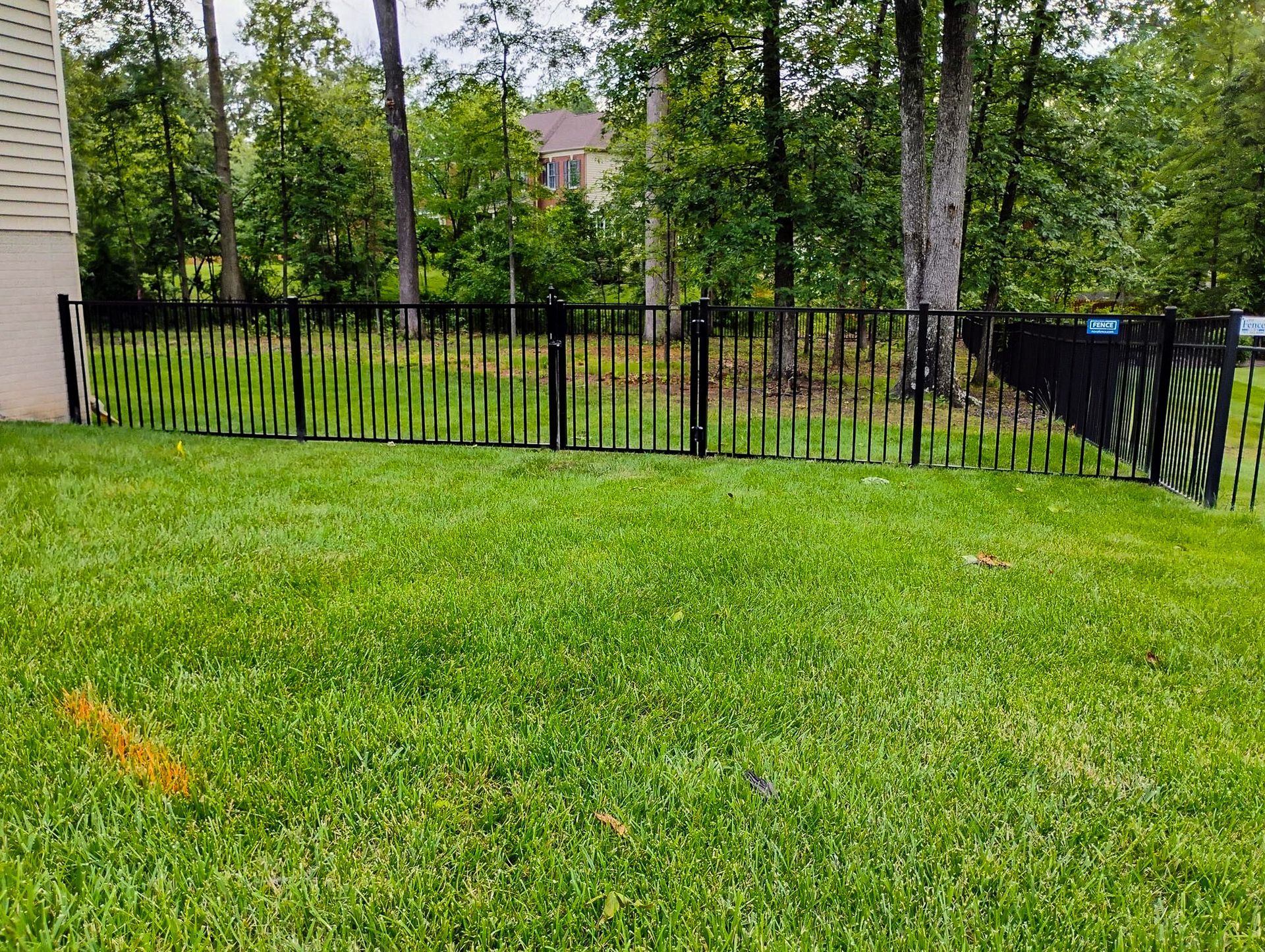 Black metal fence encloses a green lawn with trees in the background.