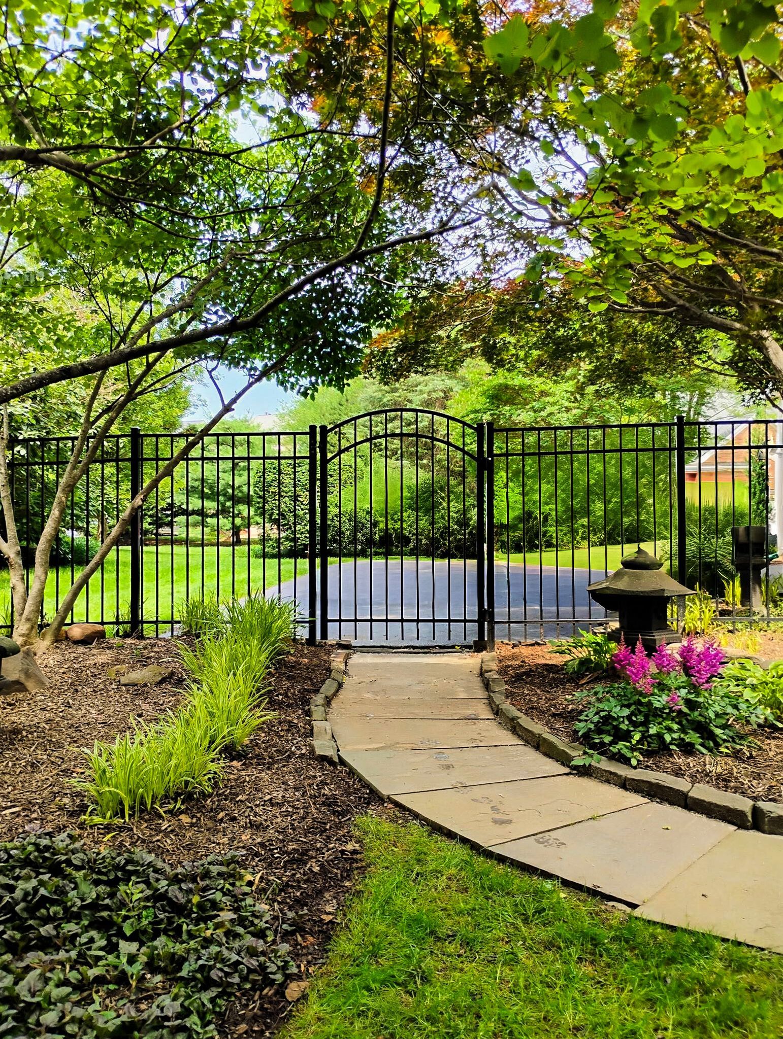 Stone path leads to a black wrought iron gate within a lush green garden.