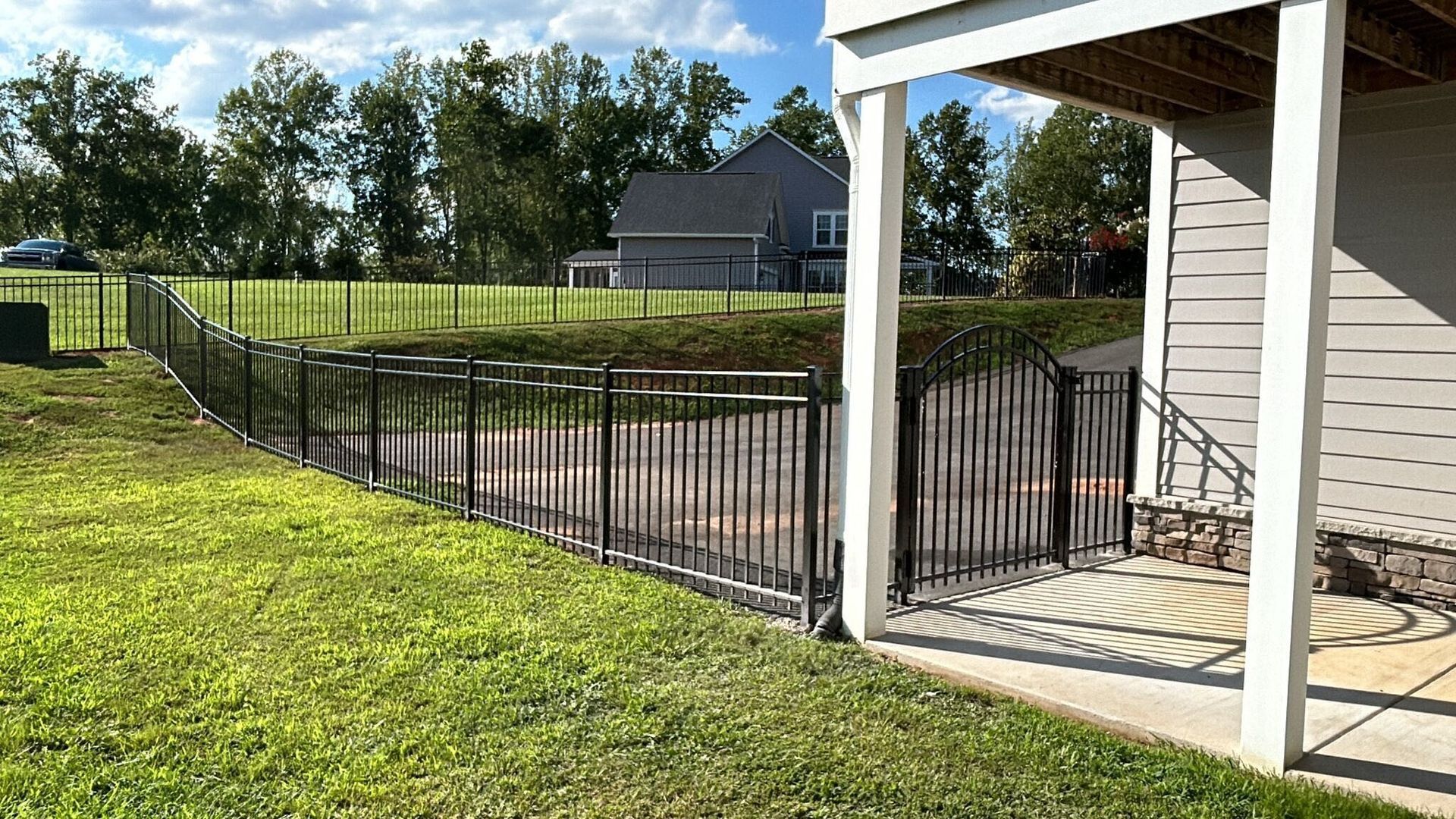 Black metal fence surrounding a yard with grass, a house in the background, and under the porch.