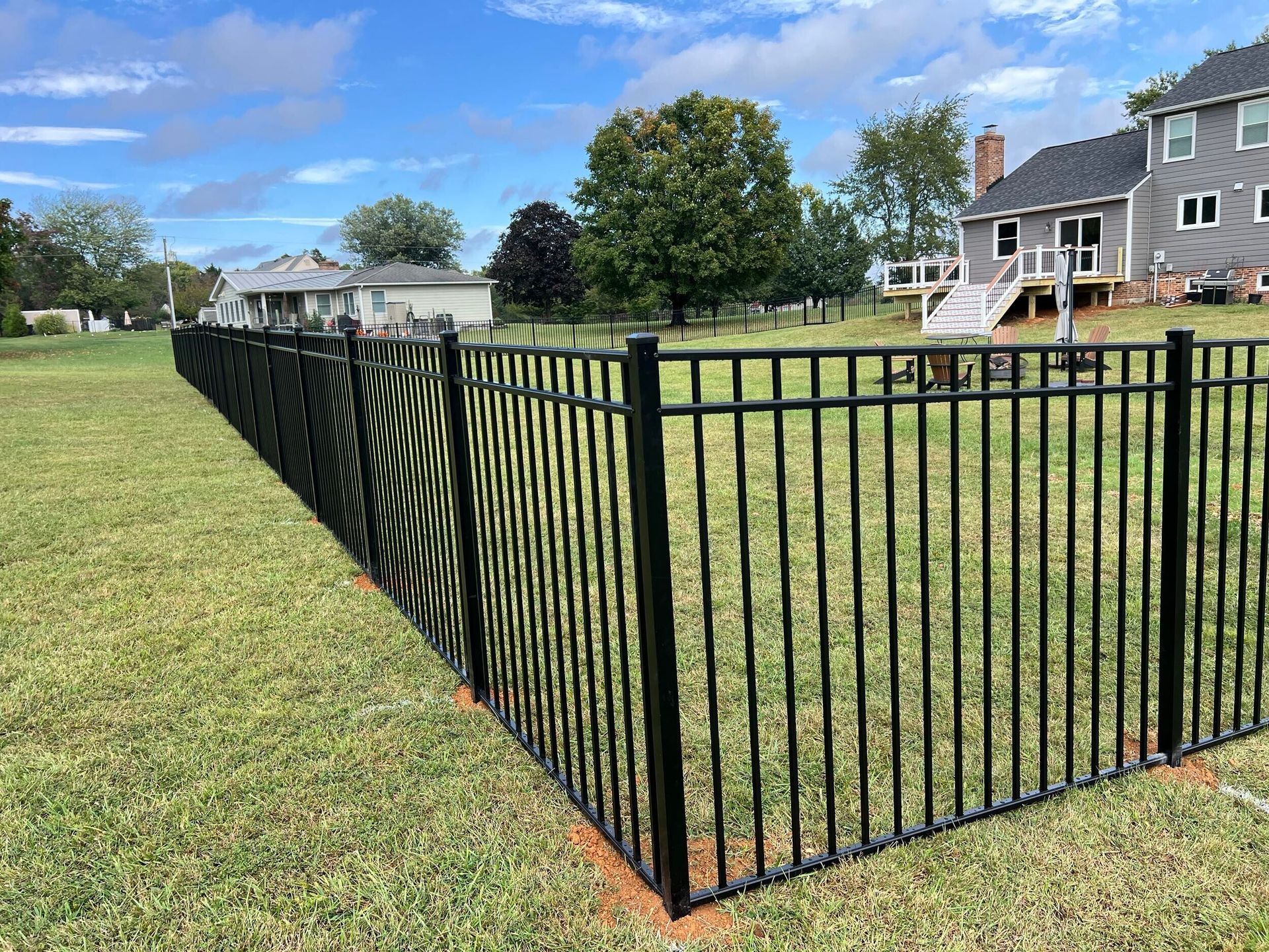 Black metal fence surrounding a grassy yard with houses in the background under a blue sky.