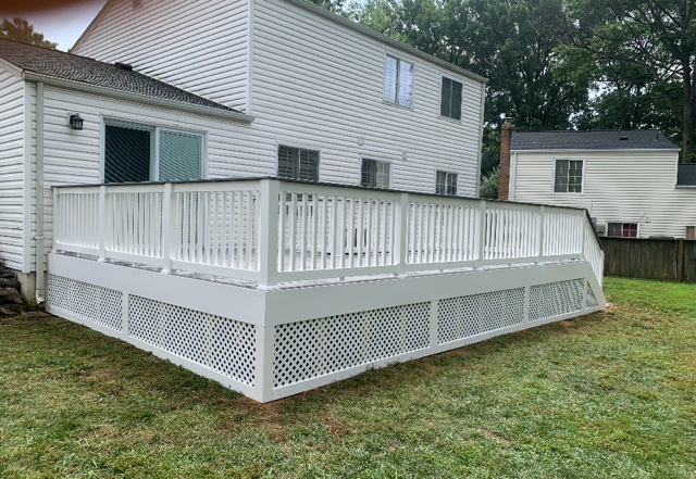White wooden deck attached to a two-story white house; surrounded by green grass.
