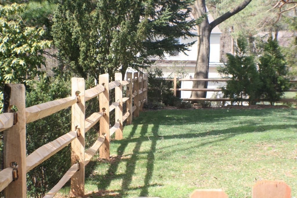 Wooden split-rail fence in a grassy yard, trees in the background, sunny day.