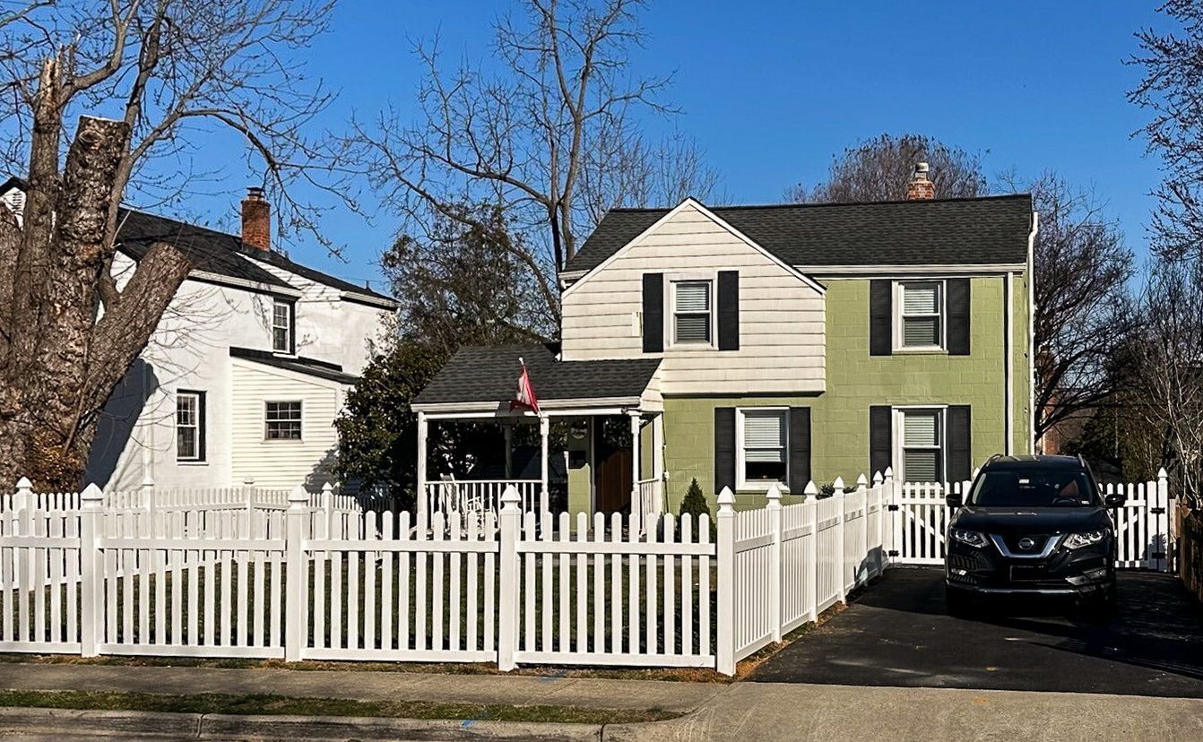 Two-story green house with white picket fence and a car parked in the driveway.