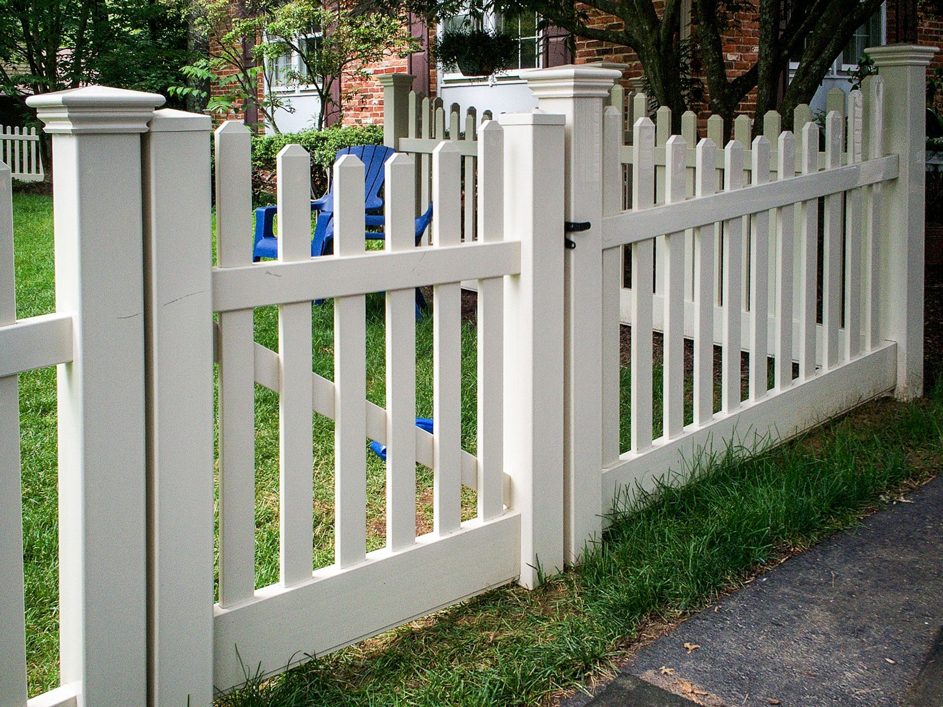 White picket fence with gate in front of a green yard and sidewalk.