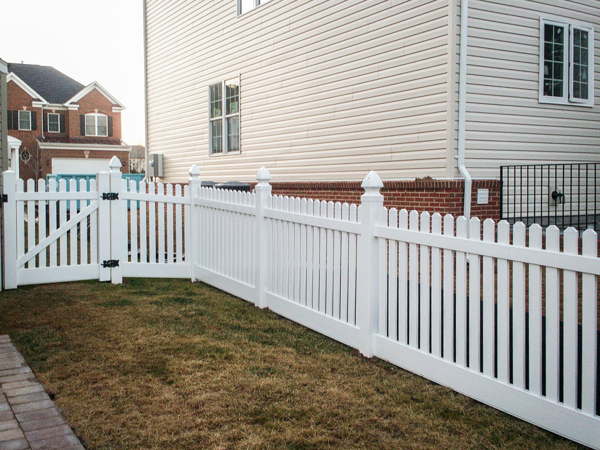 White picket fence surrounds a backyard with a house. Gate visible.