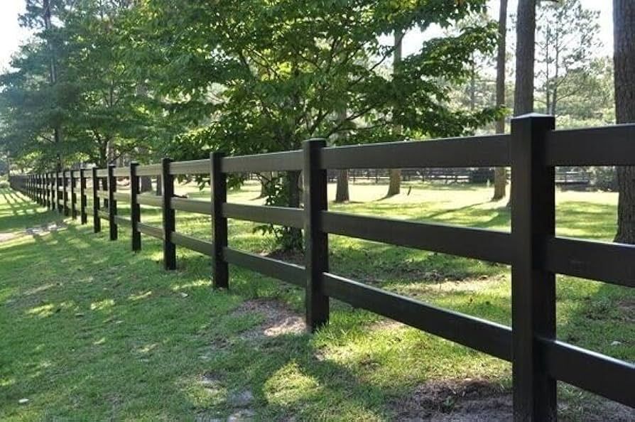Black wooden fence in a grassy area, with trees in the background.