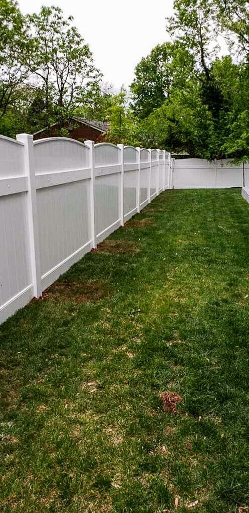 White vinyl fence in a grassy backyard, trees in the background, overcast sky.