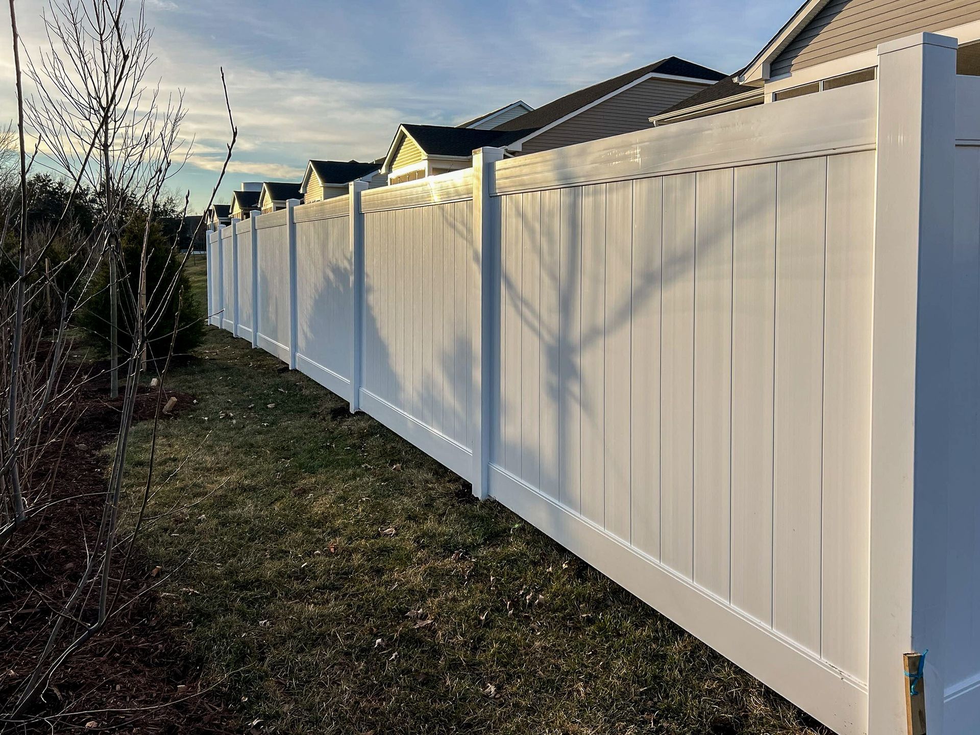 White vinyl fence along grassy yard, houses in background under blue sky.