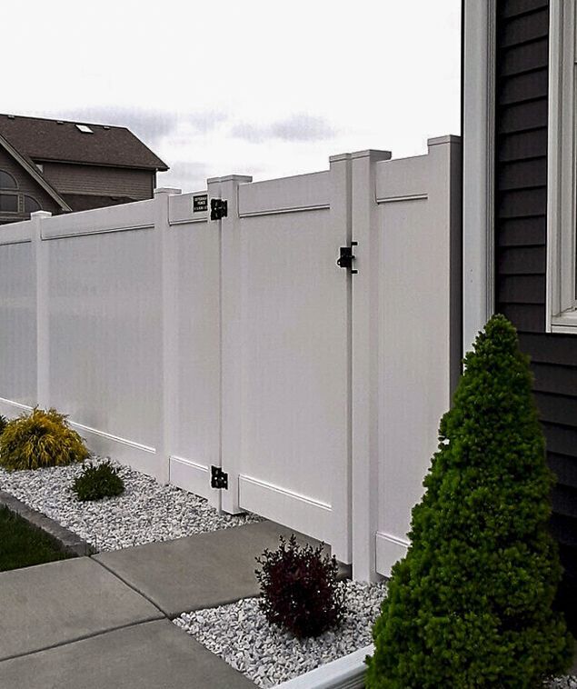 White vinyl fence with gate, along a sidewalk and garden.