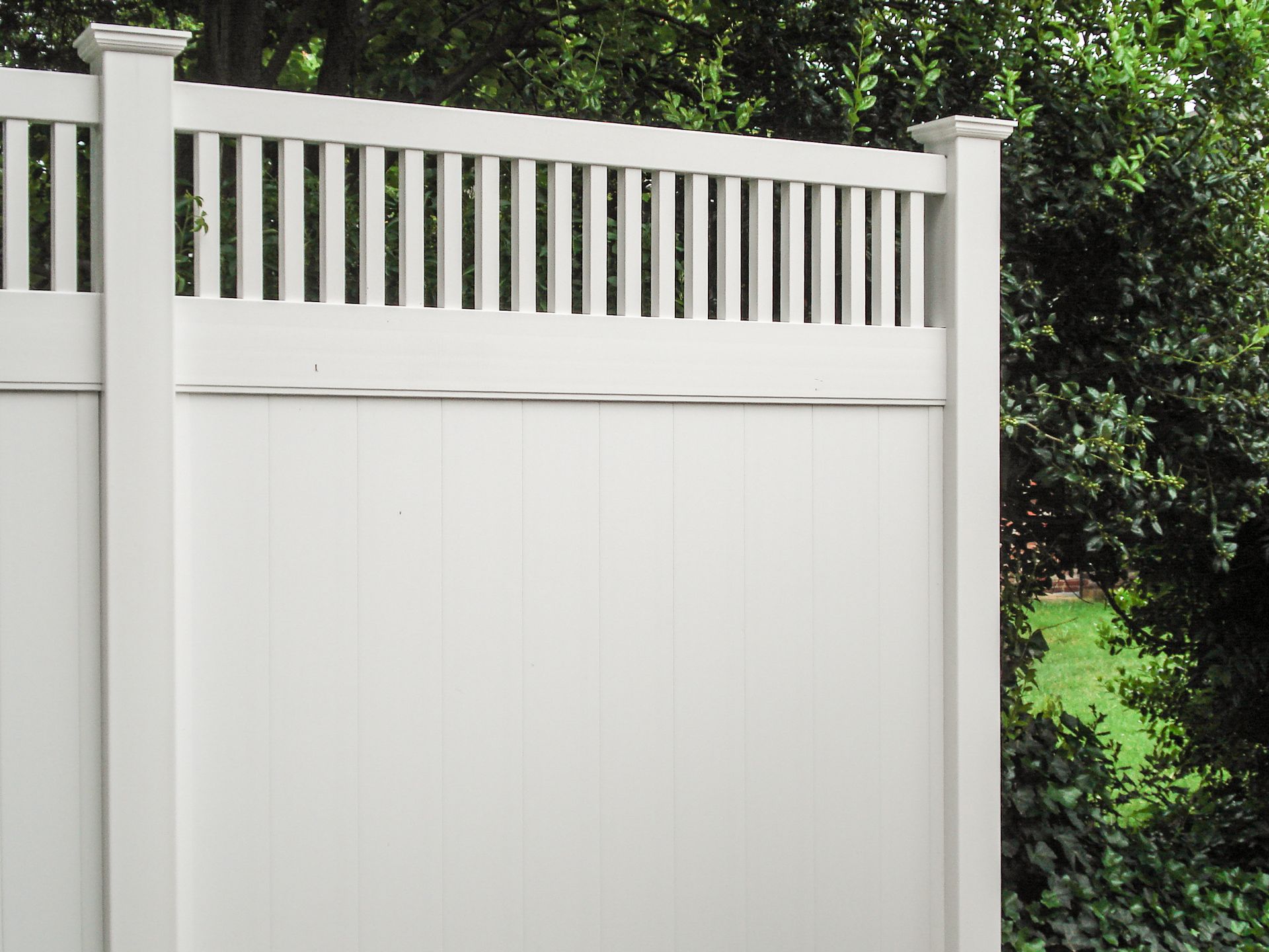 White privacy fence with vertical slats and open top, set against green foliage.