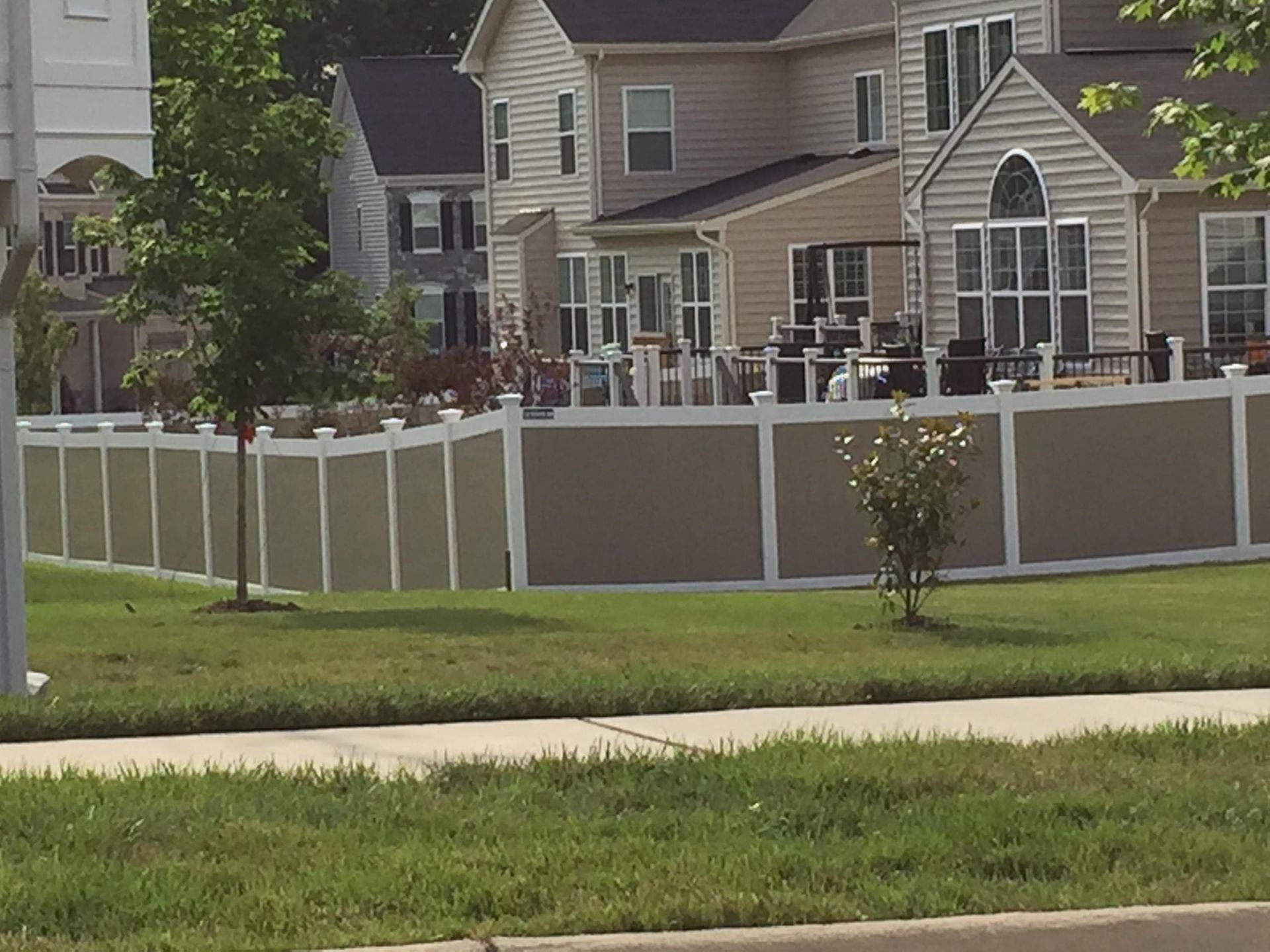 Brown and white privacy fence surrounds homes with decks and windows, sunny day.