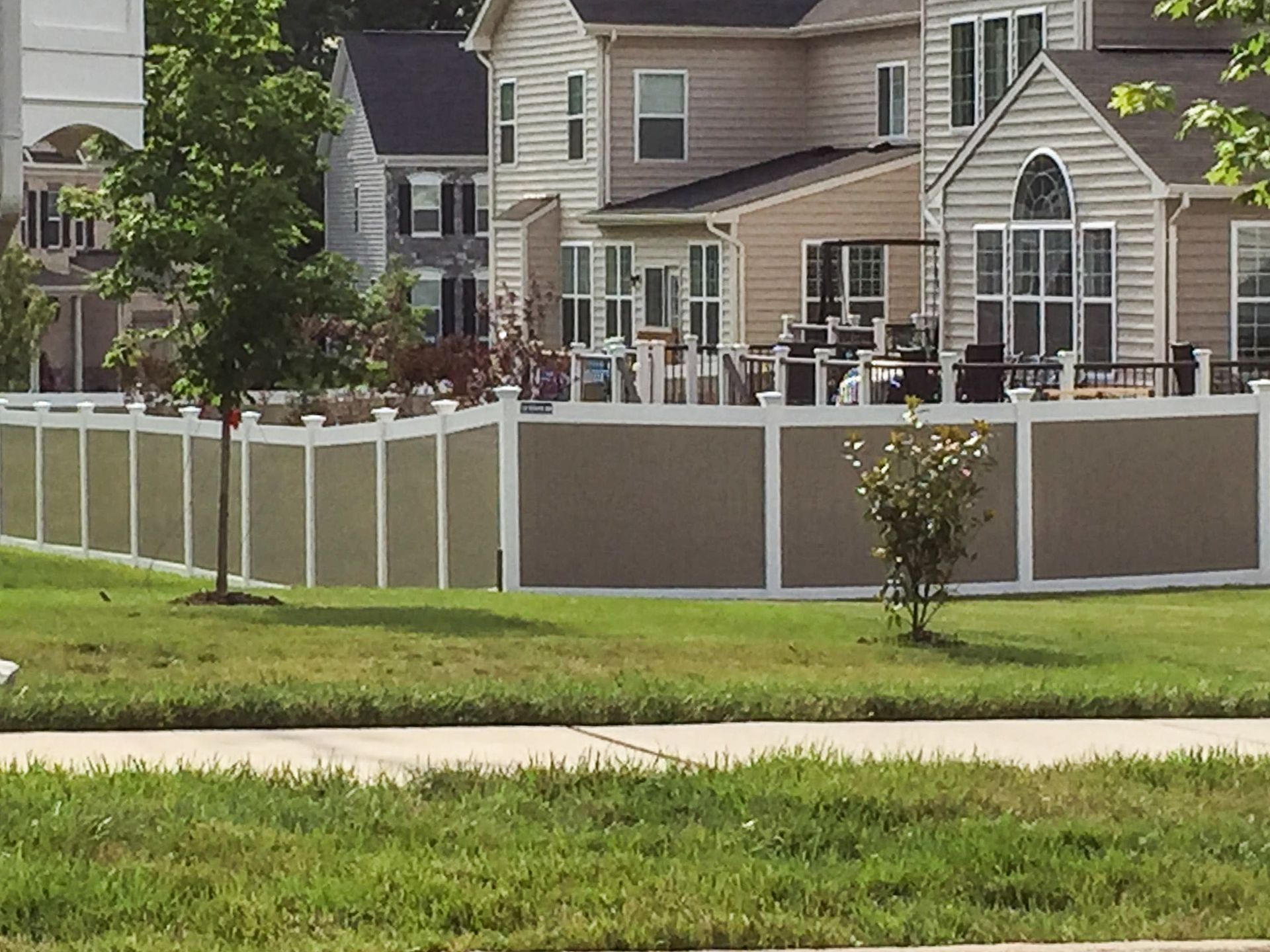 Beige and white privacy fence surrounding a backyard with several houses visible.