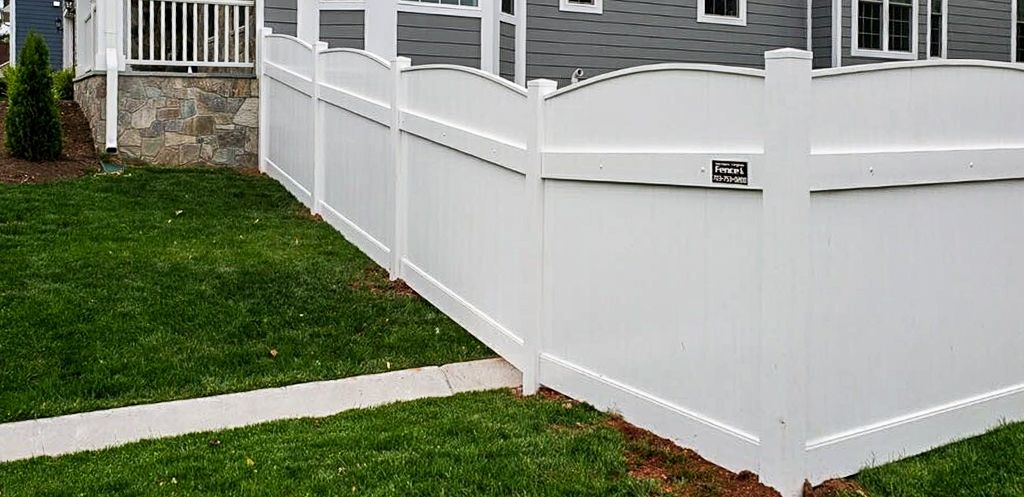 White vinyl fence around a grassy yard in front of a house.