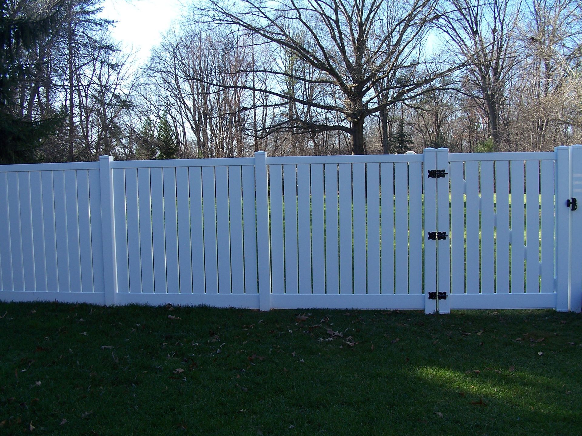 White picket fence with gate in front of trees and green grass.