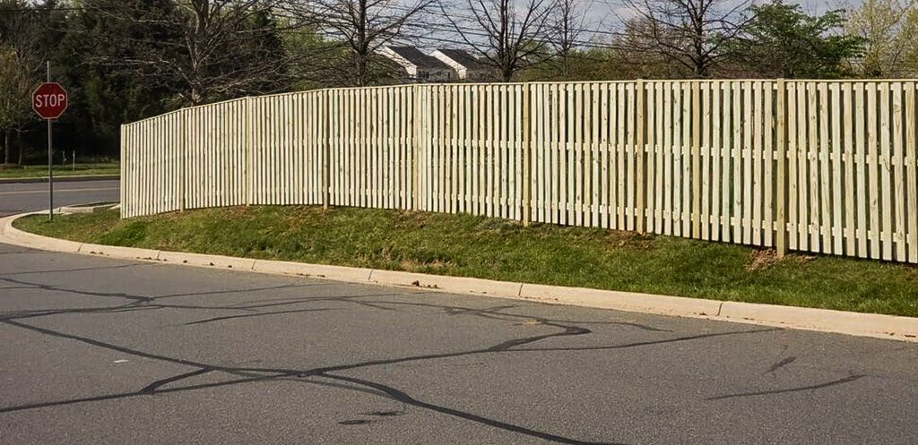A white picket fence curves along a road, with grass and a stop sign on the left.