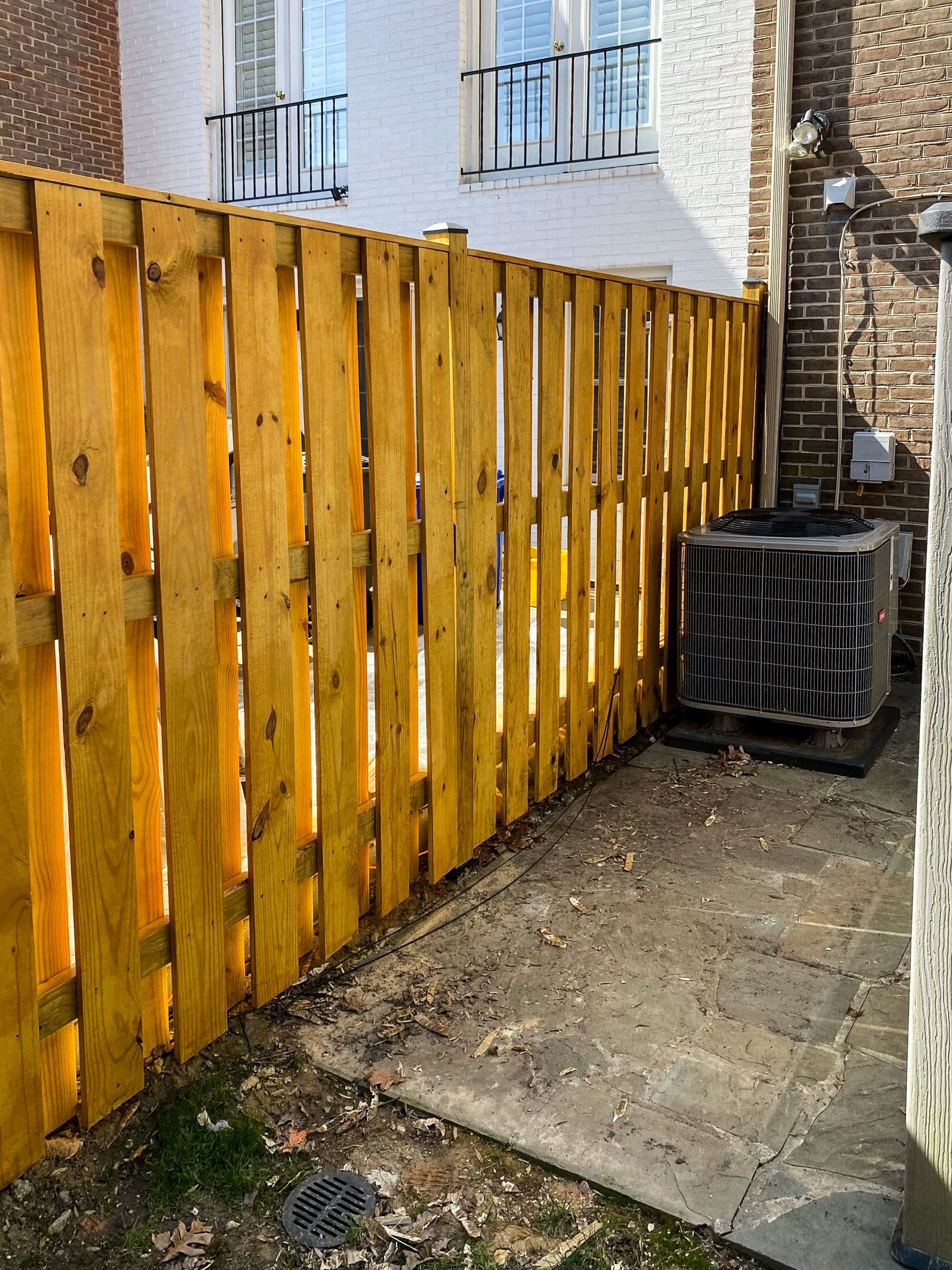 Yellow wooden fence next to an air conditioning unit and concrete patio.