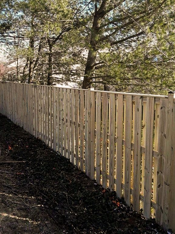 Wooden picket fence bordering a yard with dark mulch; trees in background.