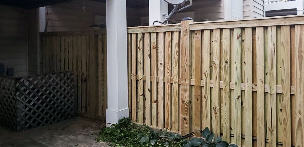 A wooden fence and white column with some greenery at the base.