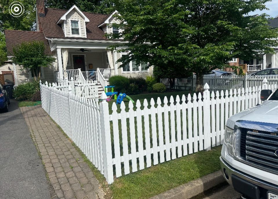 White picket fence surrounds a light-colored house with a porch and green lawn. A truck is parked on the right.