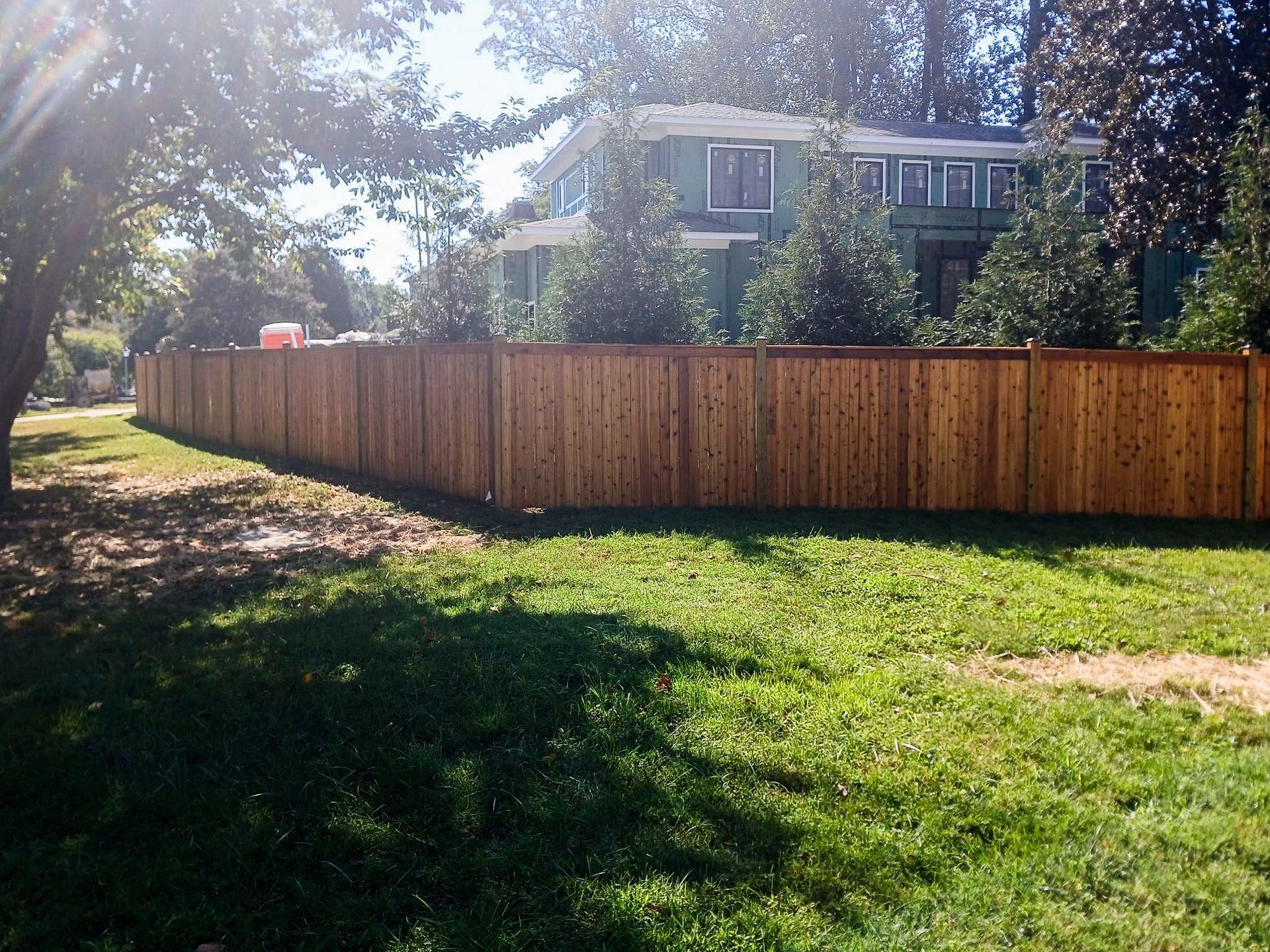 Wooden fence in front of a green-sided house on a sunny day.