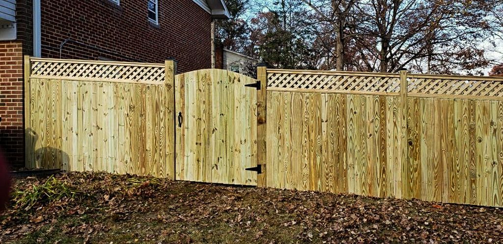 Wooden fence with gate, topped with lattice, in front of a brick building.