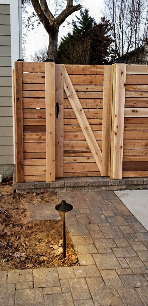 Wooden gate with diagonal support. Brick path and landscape lighting.