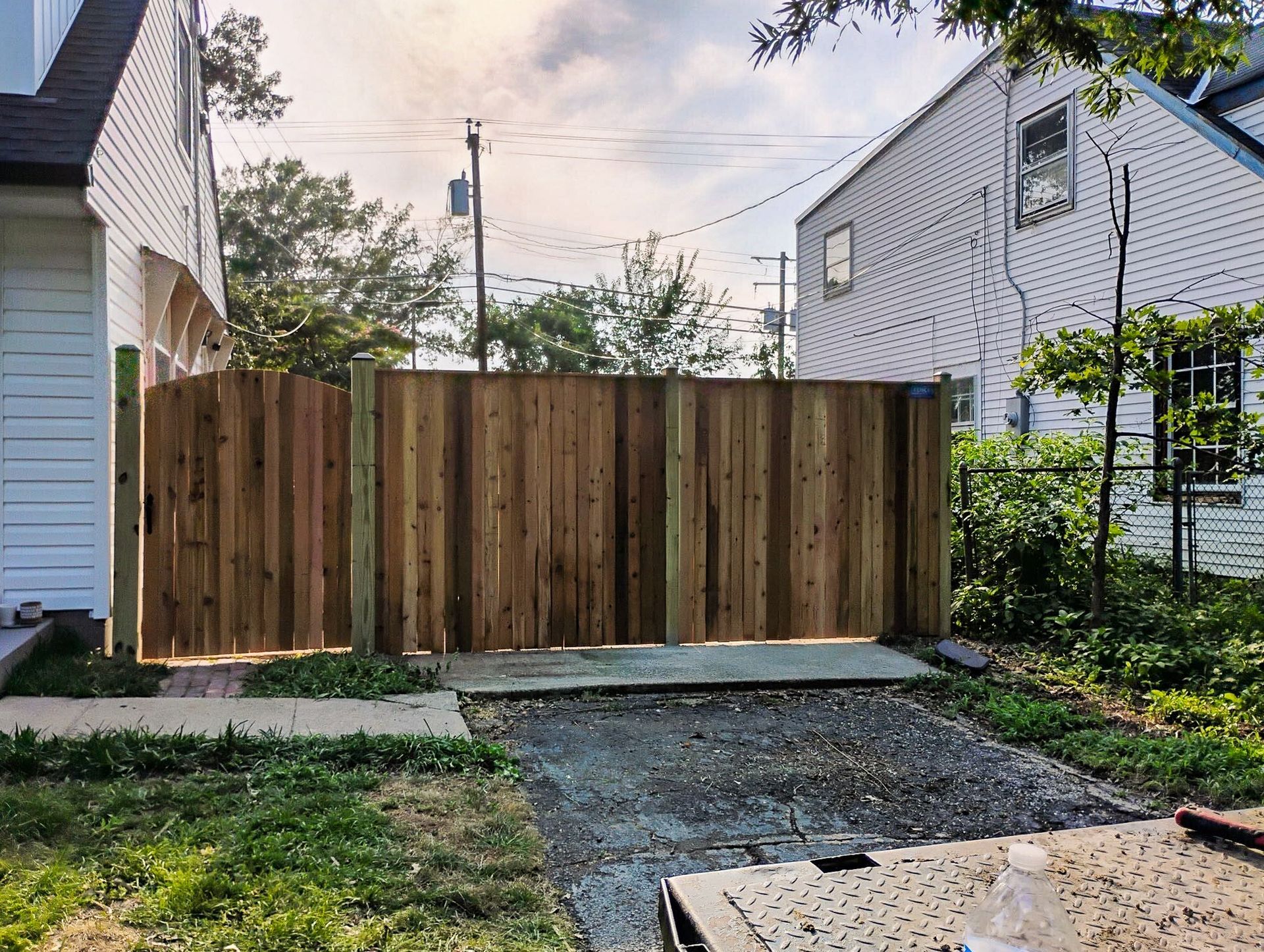Wooden privacy fence between two houses. Driveway in front, with green grass to the left and right.